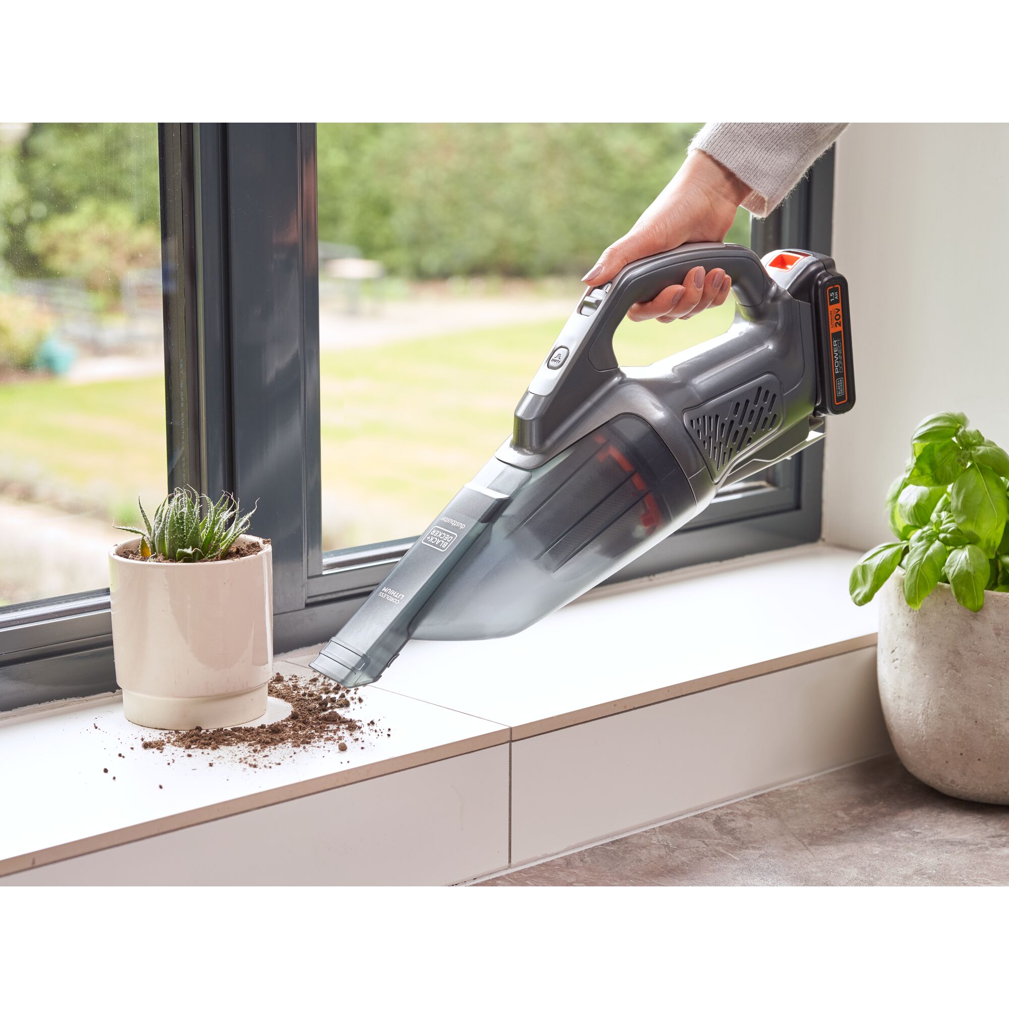 BLACK+DECKER BCHV001D1E handheld vacuum cleaning soil near a plant on a windowsill indoors.