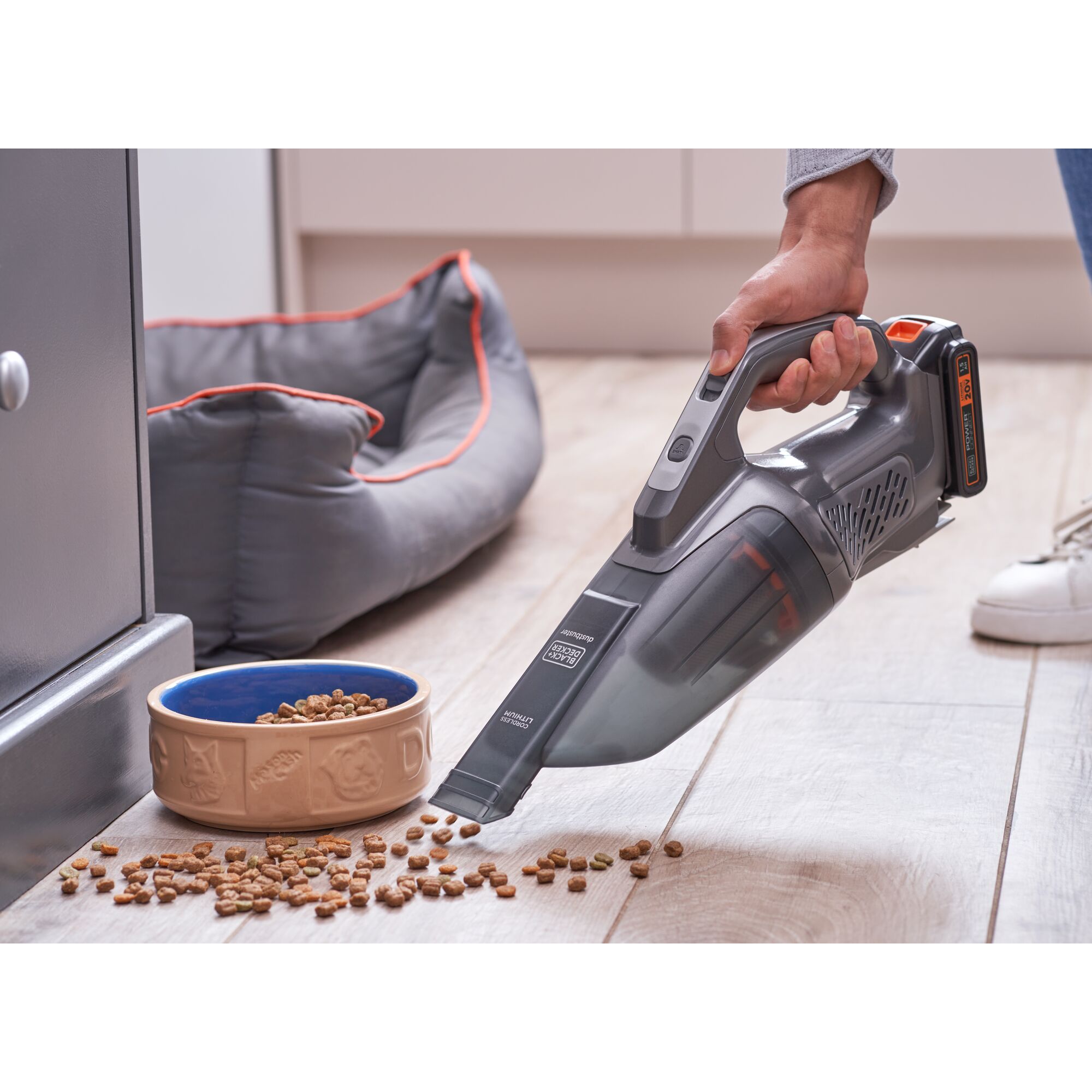 BLACKDECKER BCHV001D1E handheld vacuum cleaning pet food near a dog bed on wooden floor, side angle.