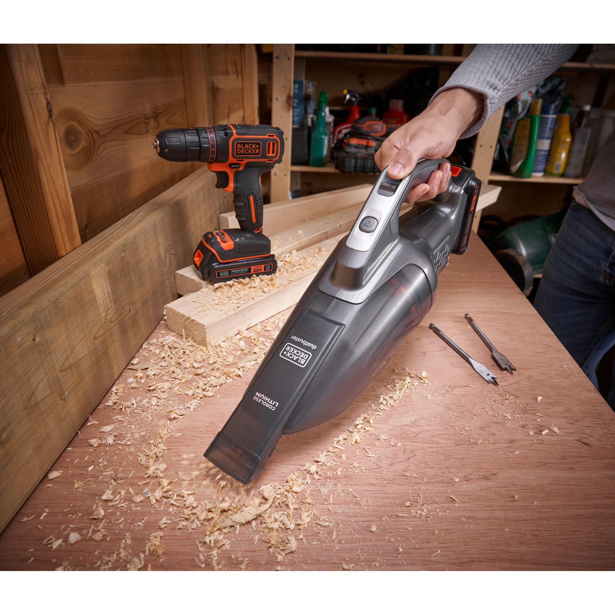 BLACK+DECKER BCHV001D1E handheld vacuum cleaning wood shavings on a workbench, with a drill and drill bits nearby.
