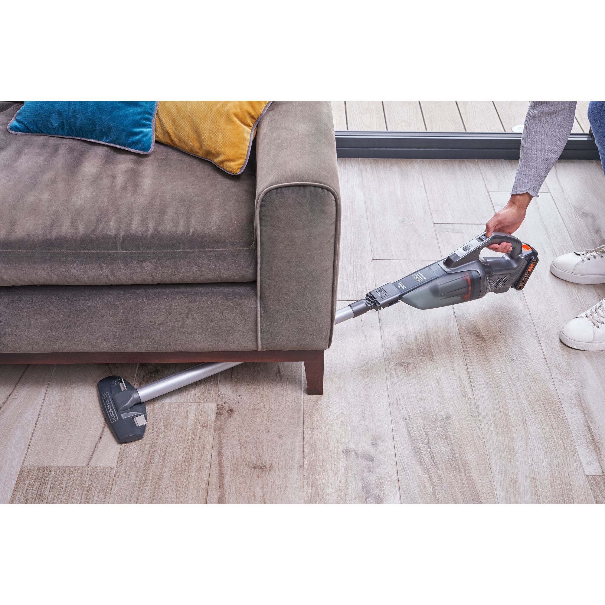 BLACKDECKER BCHV001D1E cordless stick vacuum cleaning under a brown sofa on wooden floor.