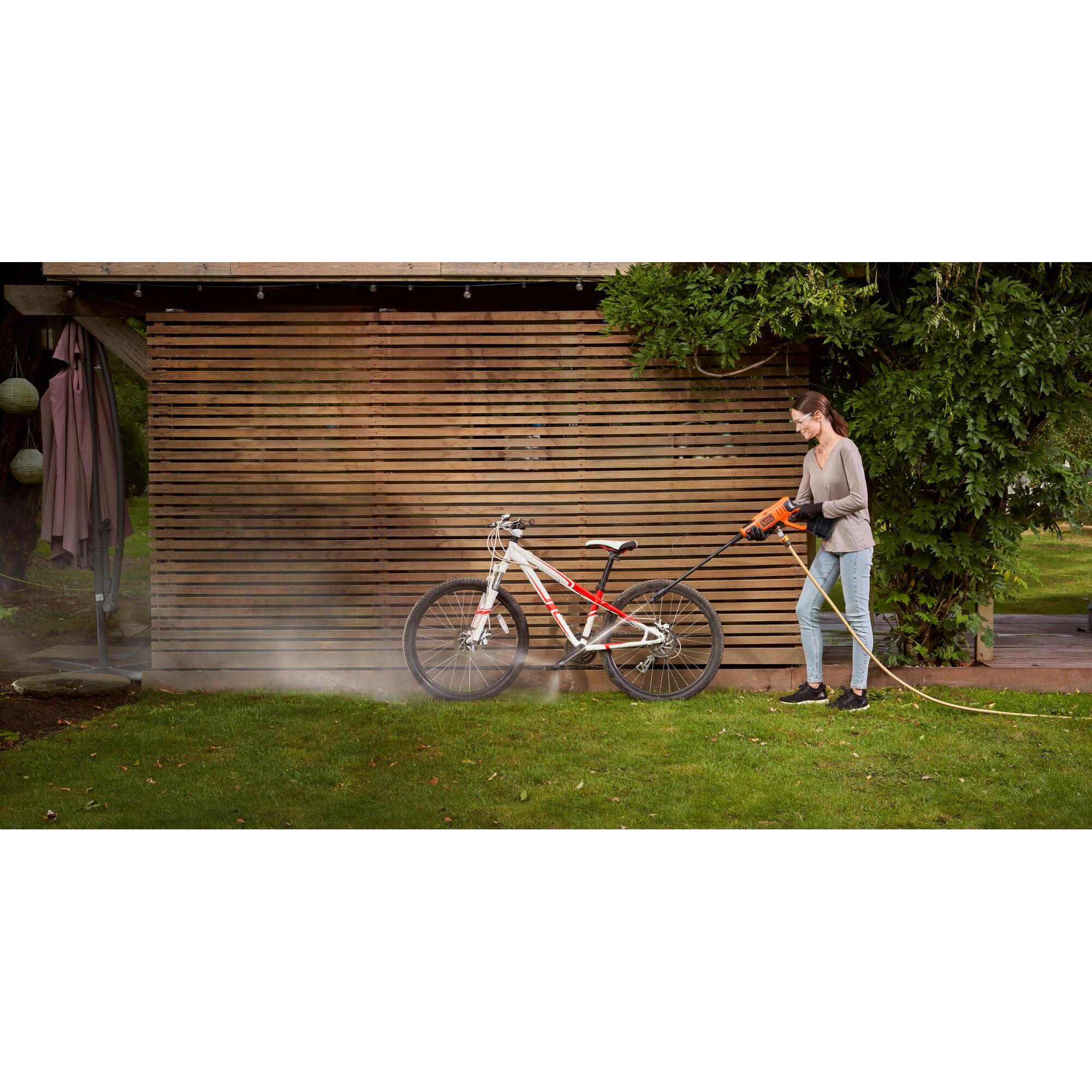 BLACKDECKER BCPC20D1 pressure washer cleaning a white and red bicycle outdoors on grass.