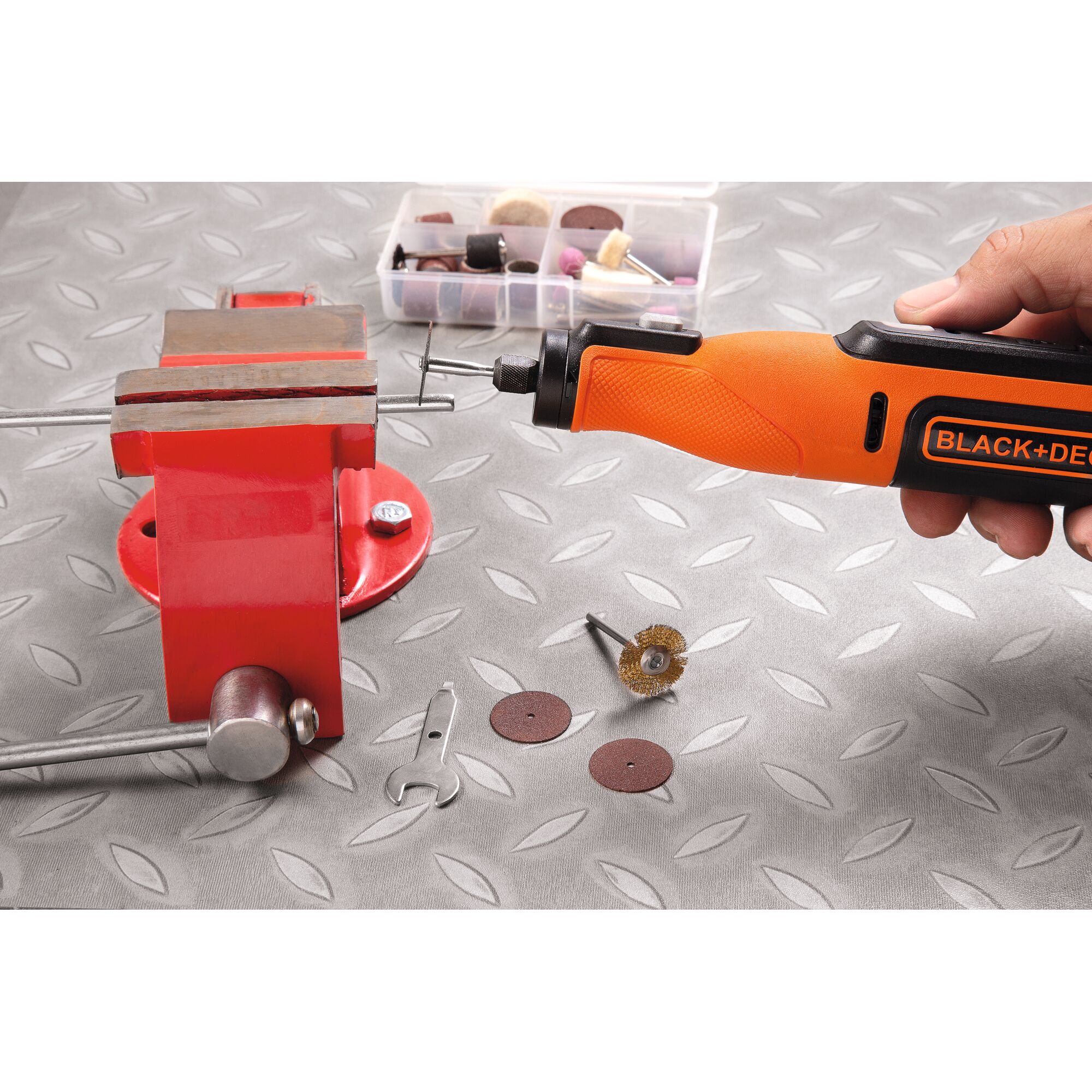 BLACKDECKER BCRT8K35 rotary tool in hand near a red vise with accessories on a metal surface.