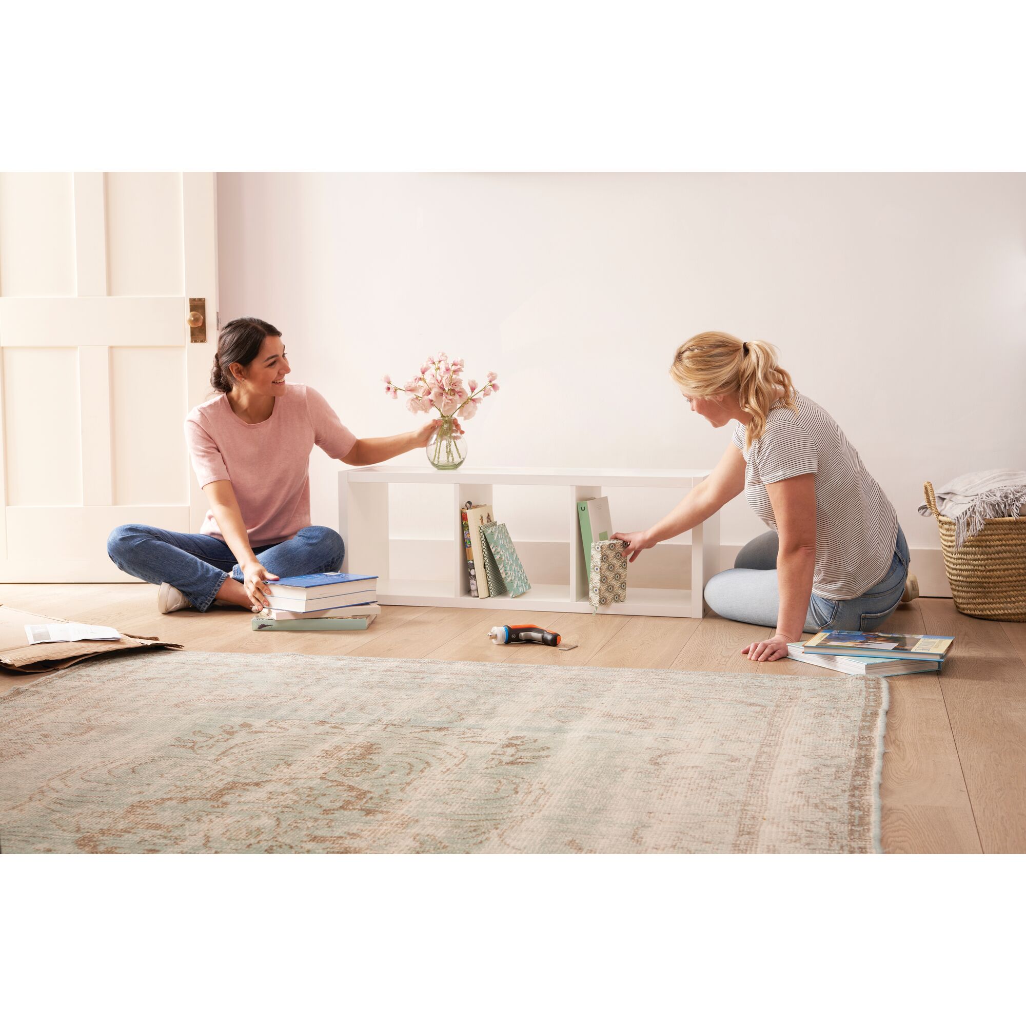 BLACKDECKER BCRTA601 cordless screwdriver on wooden floor between two people organizing books and shelves in a living room.