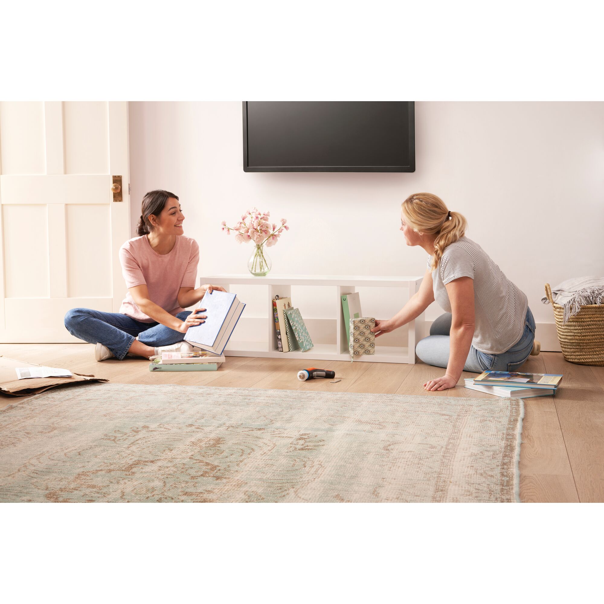 BLACKDECKER BCRTA601 cordless screwdriver on floor as two people organize books on a white shelf in a living room.