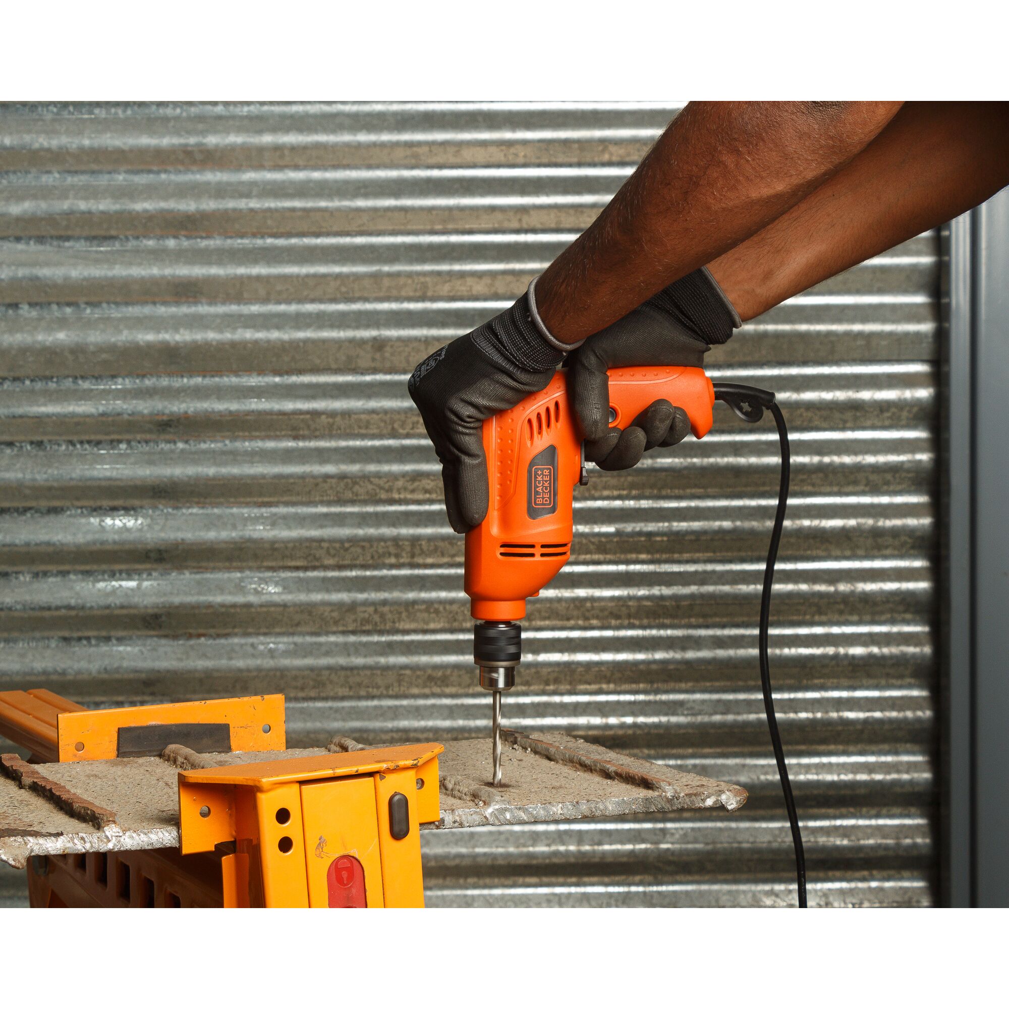 BLACKDECKER BD10RD electric drill in use on metal surface, orange body, gloved hand, power cable visible.
