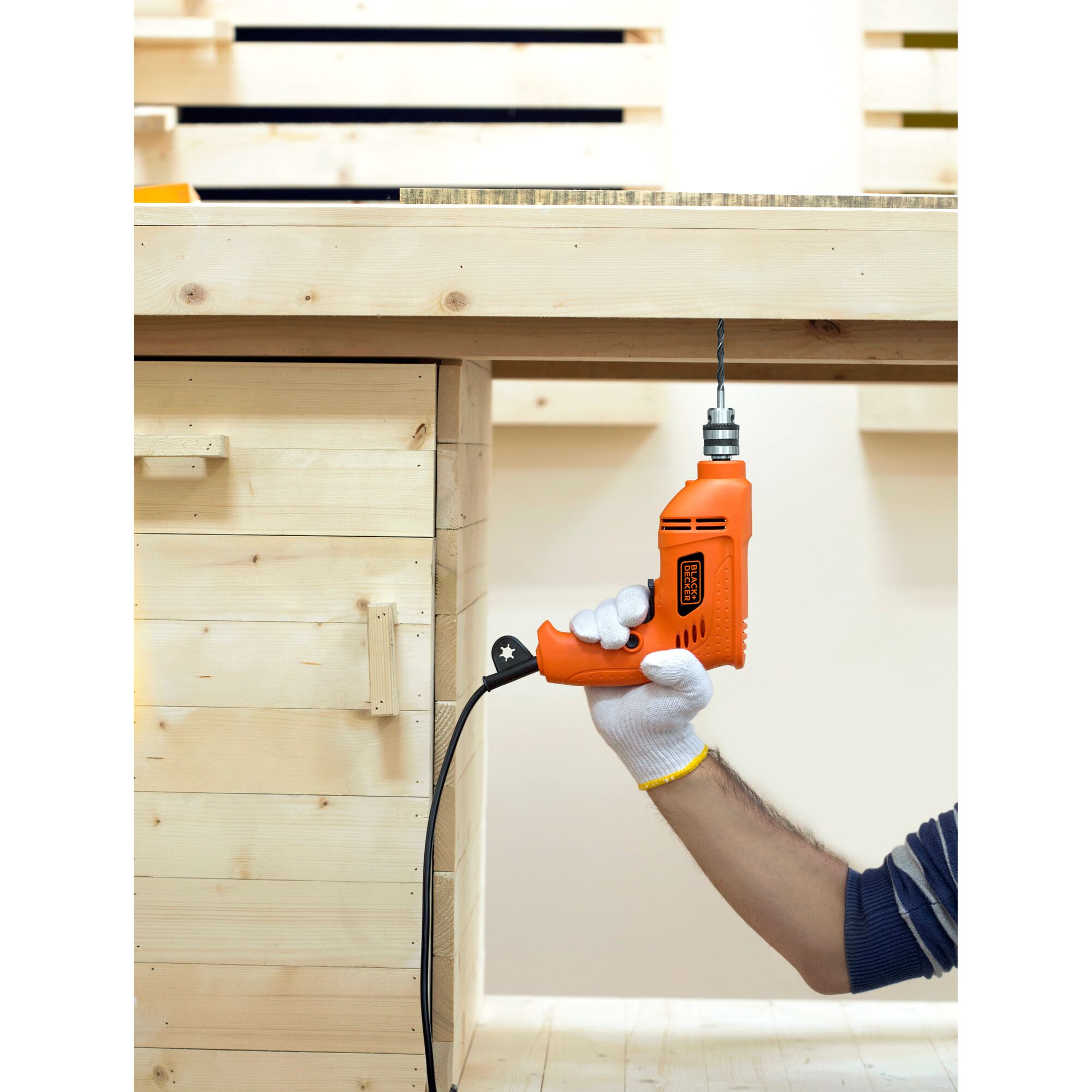 BLACKDECKER BD65RD orange corded drill held under wooden table, side angle, drill bit attached.