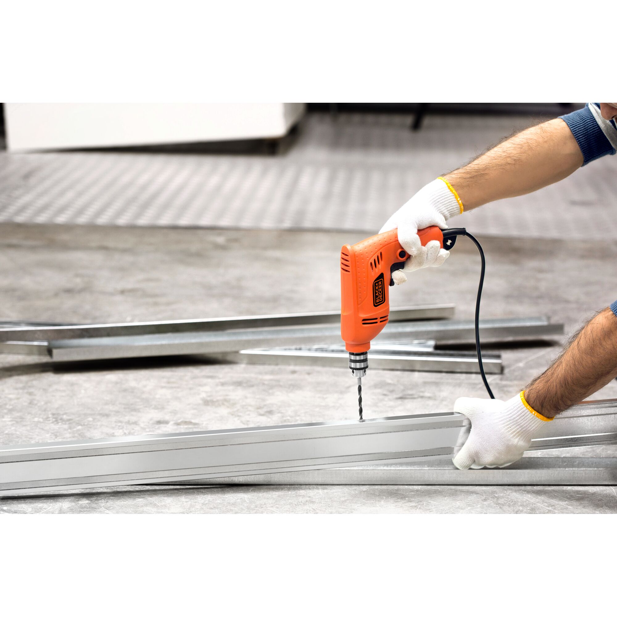 BLACKDECKER BD65RD corded drill used on metal beams in workshop, photo shows close up of hands and tool.
