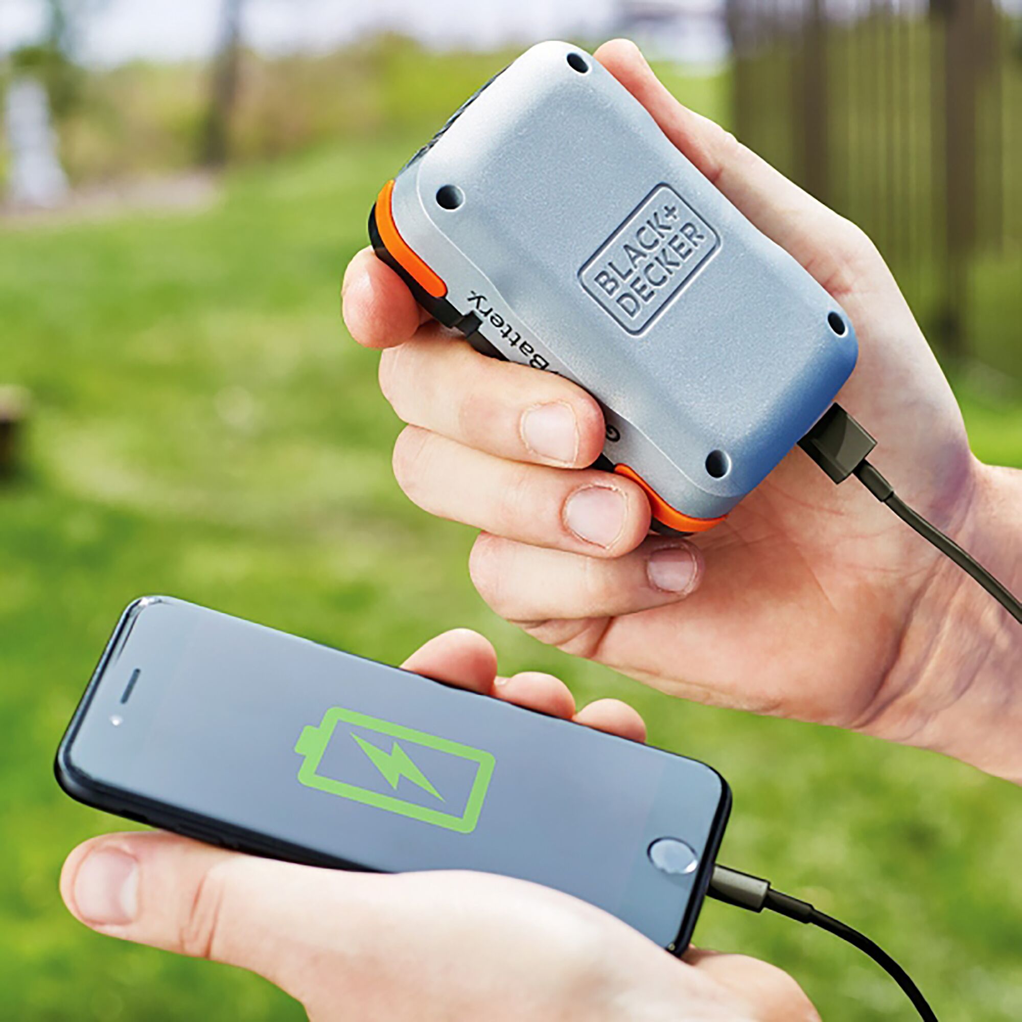 BLACK+DECKER BDCB12U portable power bank charging a smartphone outdoors, silver and orange design.