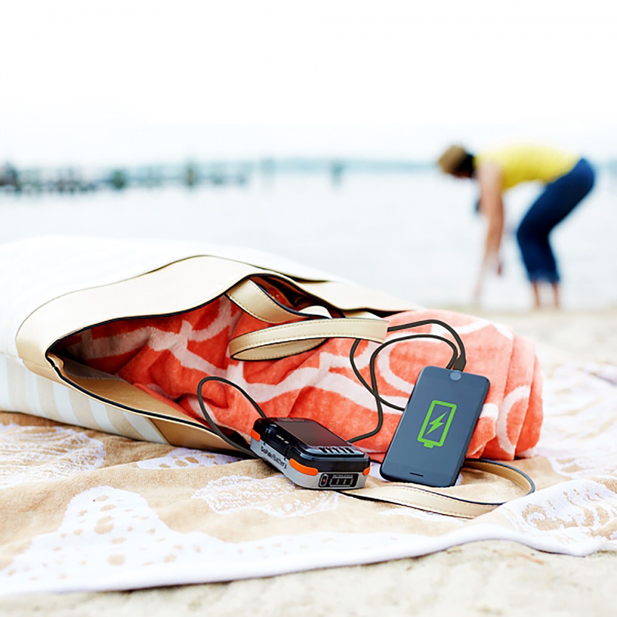 BLACKDECKER BDCB12U portable charger connected to a phone on a beach towel with a bag and blanket nearby.