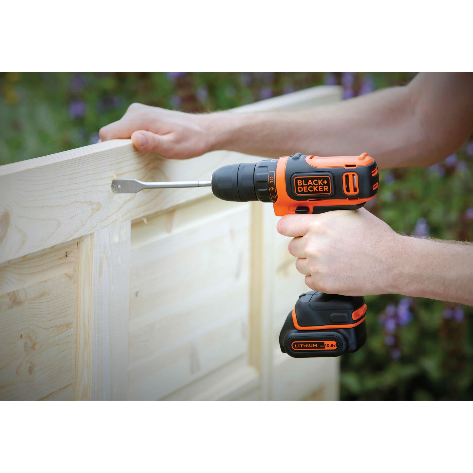 BLACK+DECKER BDCDD12 cordless drill in use on a light wood surface, orange and black color, handled by a person.