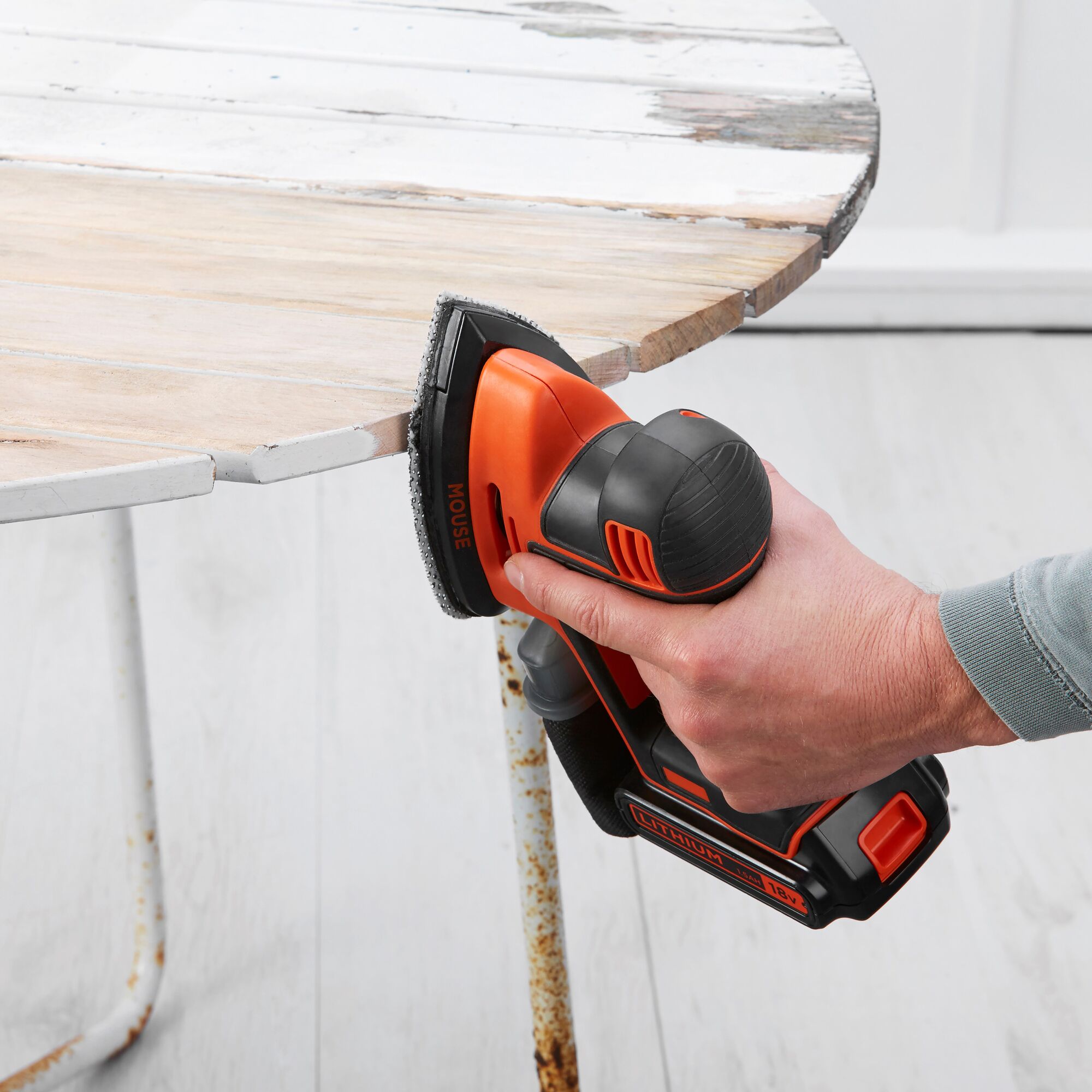 BLACKDECKER BDCDS18 cordless mouse sander sanding edge of round wooden table, side angle.