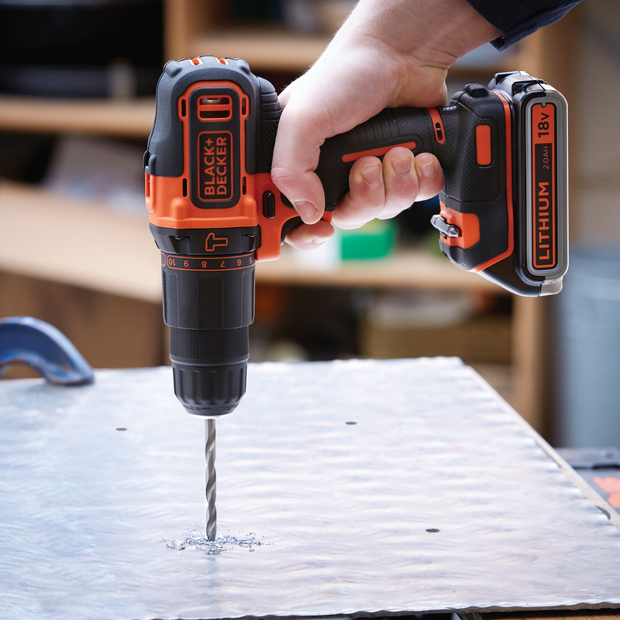 BLACK+DECKER BDCHD18K1B cordless drill in use, drilling through metal sheet, visible 18V lithium battery.