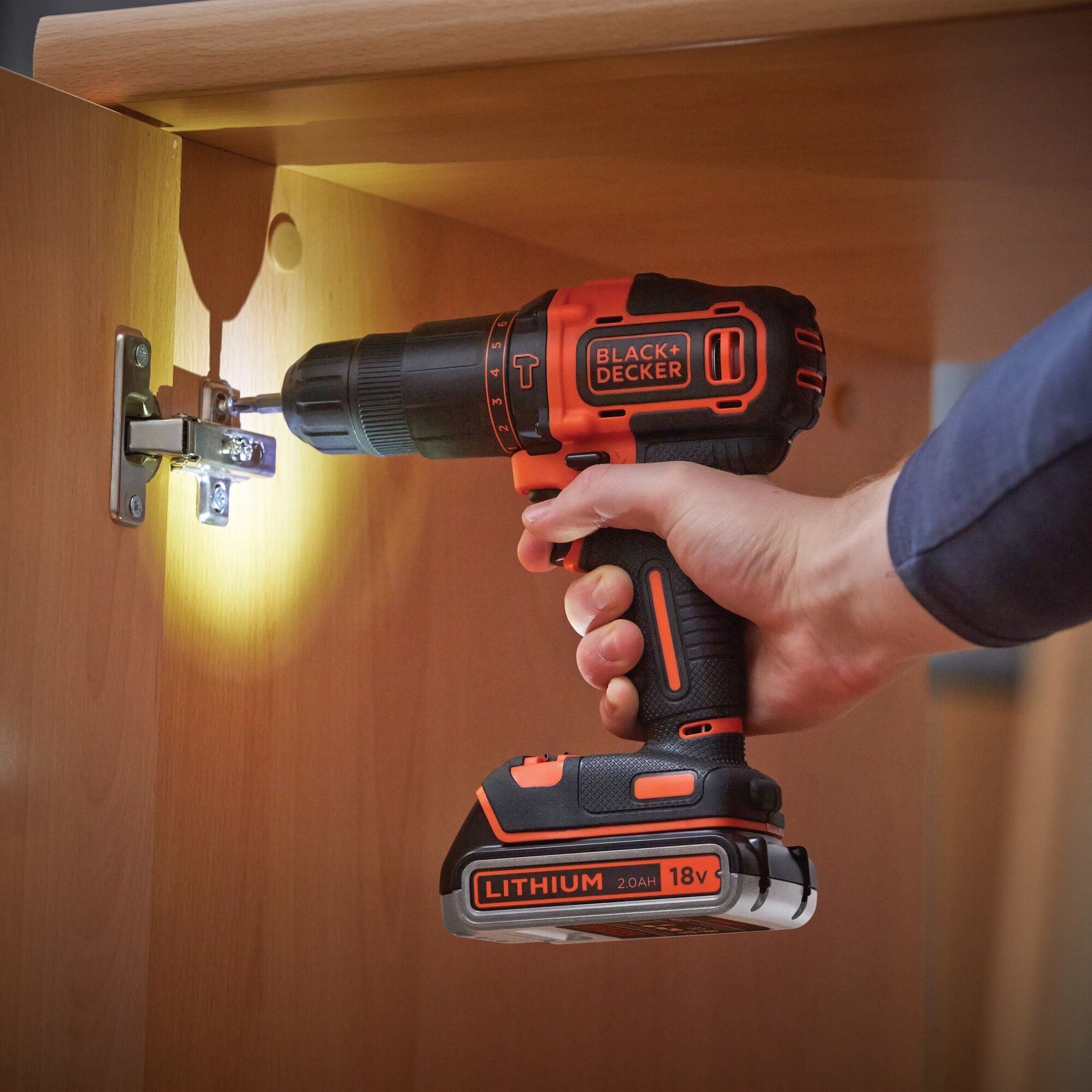 BLACK+DECKER cordless drill BDCHD18K1B in use, drilling cabinet hinge, orange and black, 18V lithium battery.