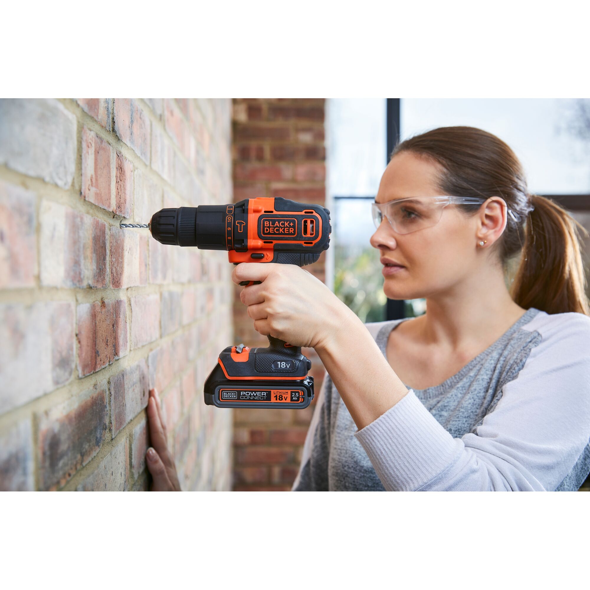 BLACKDECKER BDCHD18K1B cordless drill being used to drill into a brick wall, orange and black color.