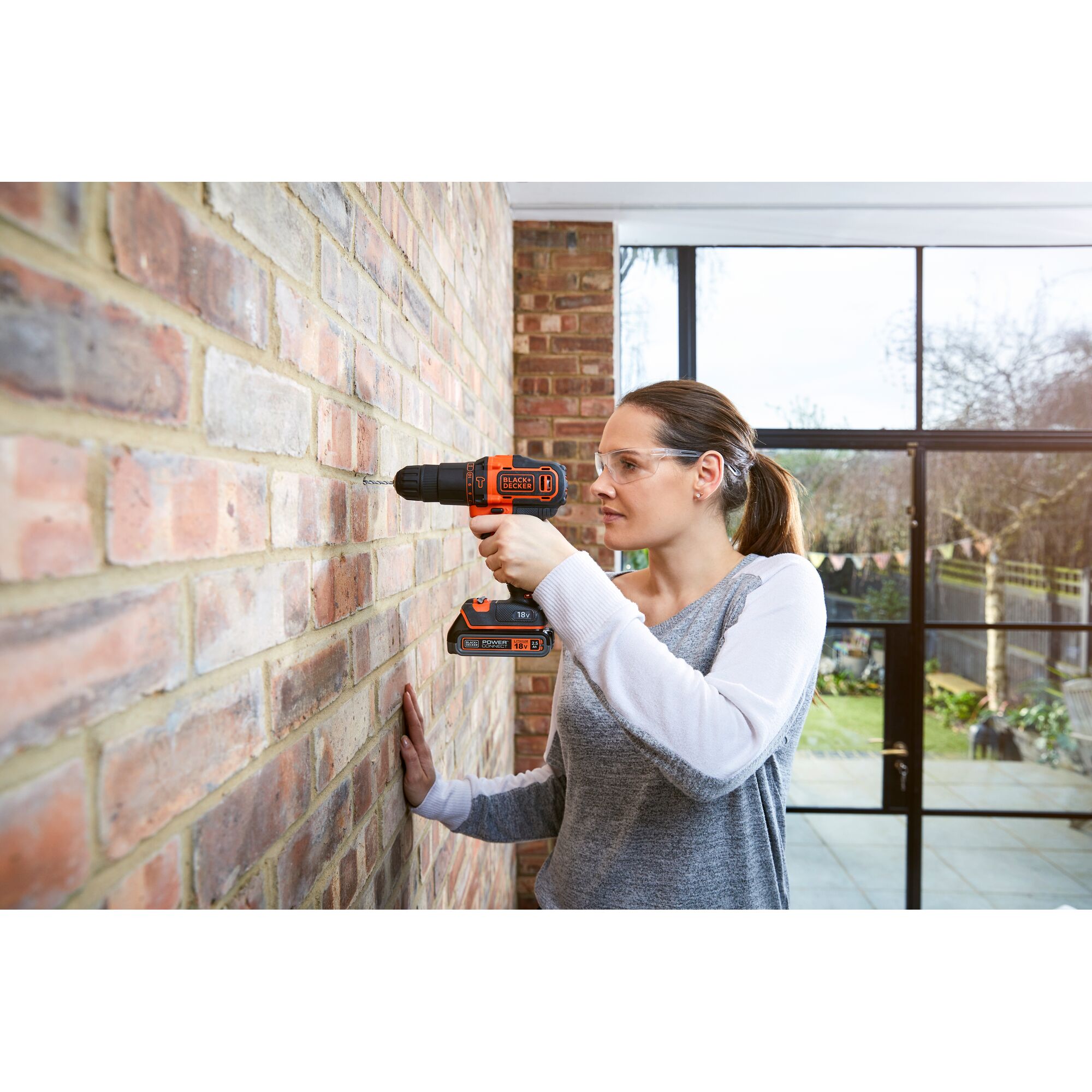 BLACKDECKER BDCHD18K1B cordless drill being used to drill into a brick wall indoors.