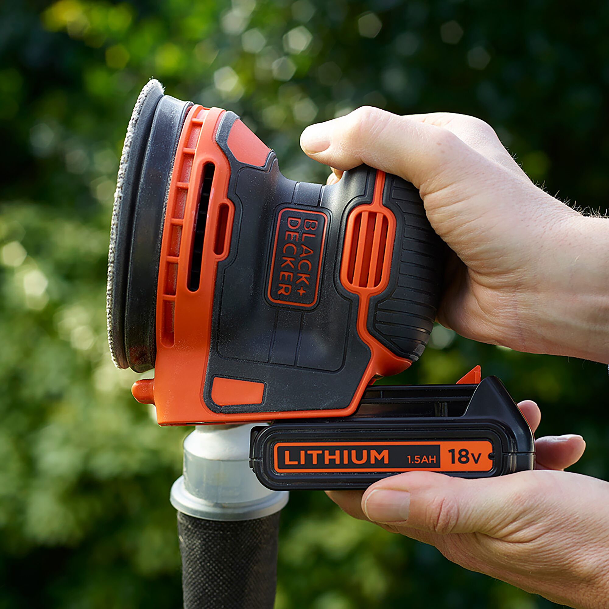 Photo of BLACKDECKER BDCROS18B cordless sander held in hand, orange and black color, 18V lithium battery.
