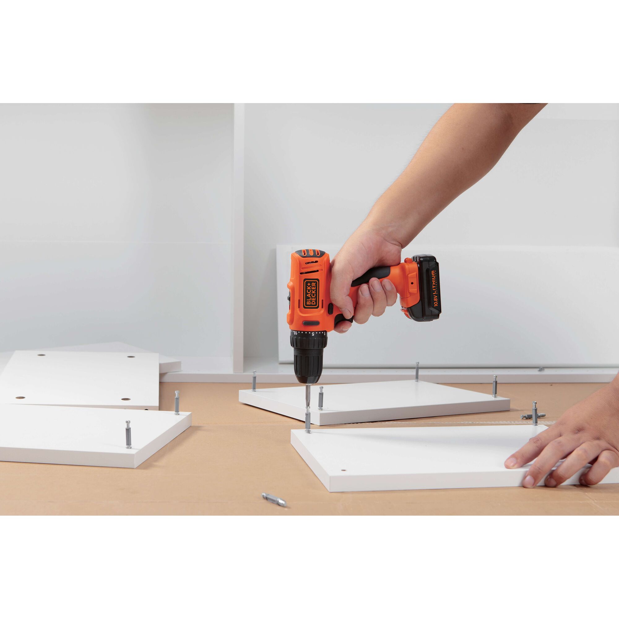 BLACKDECKER BDD12 cordless drill being used to assemble white panels on a tabletop.