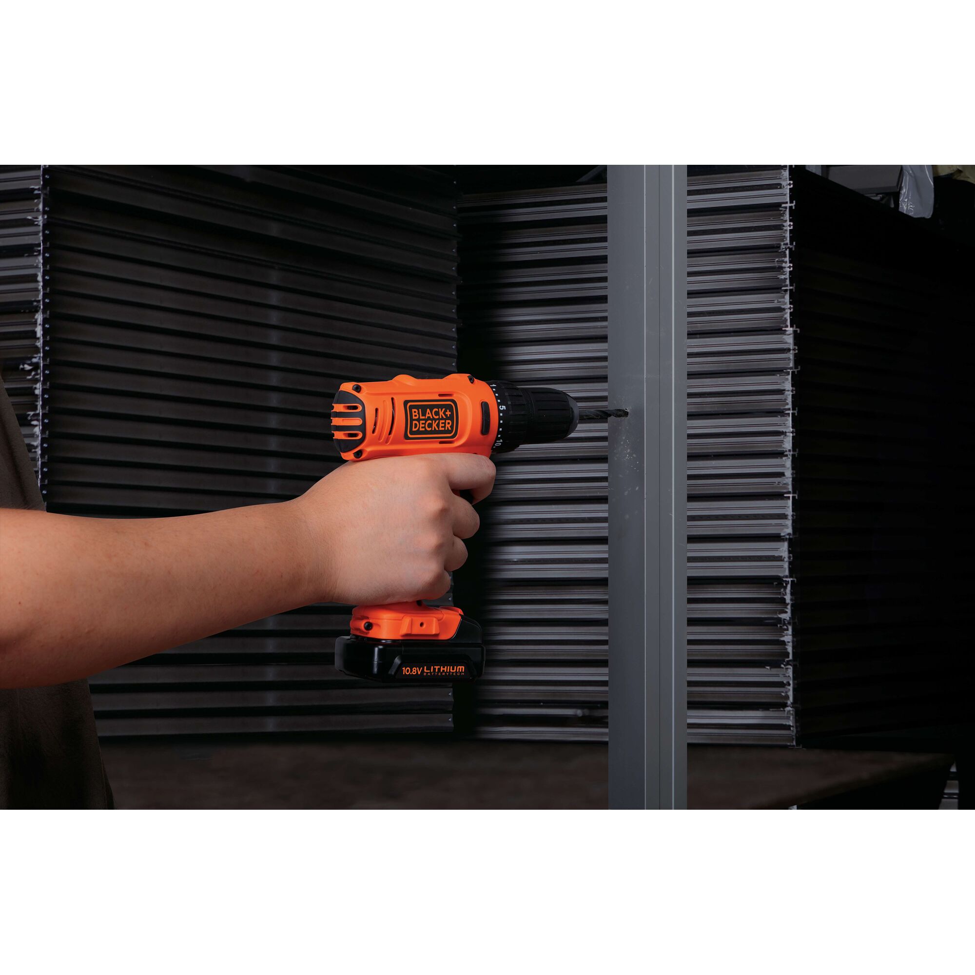 Photo of BLACKDECKER BDD12 cordless drill in use drilling into metal, orange body, 10.8V Lithium battery.