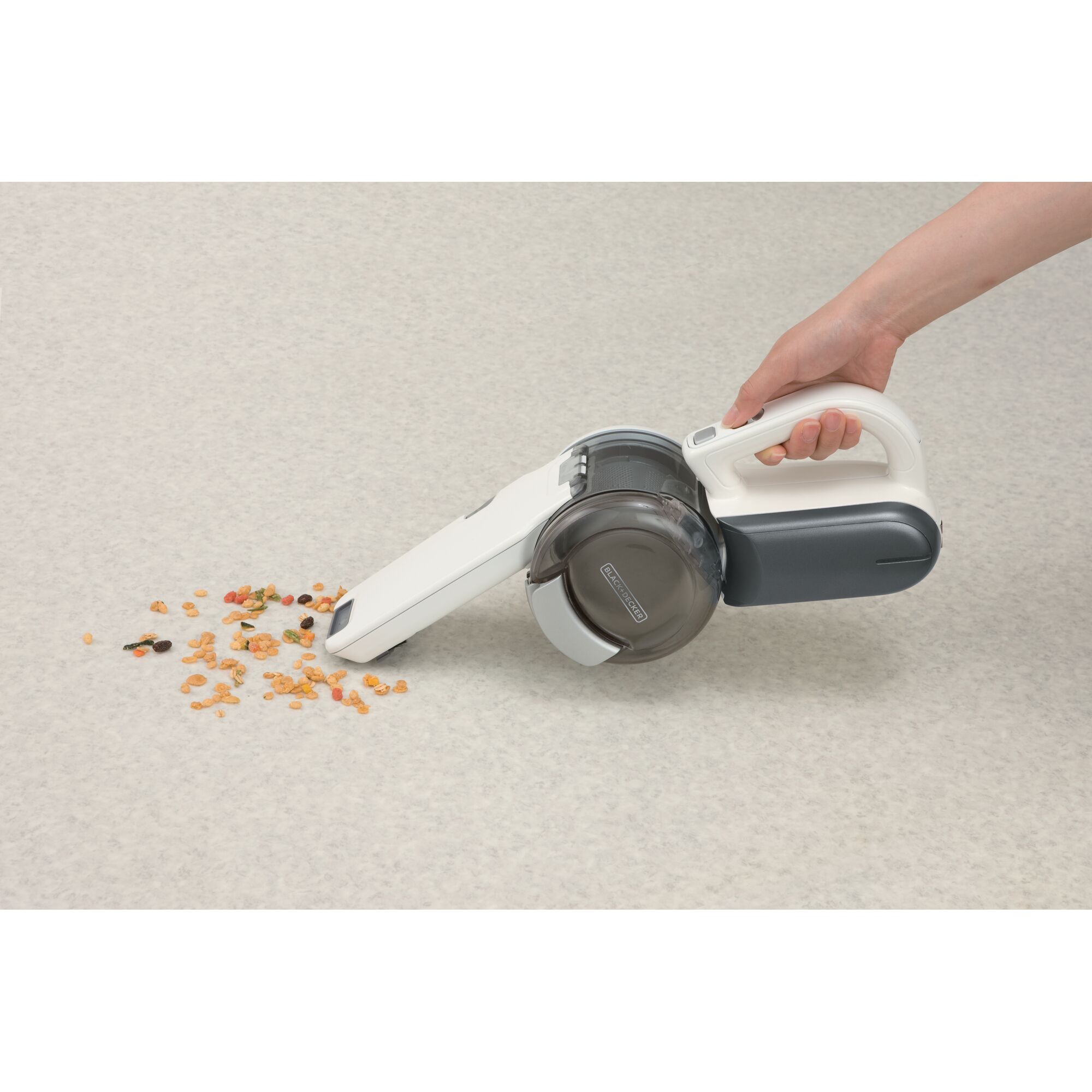 BLACK+DECKER BDH1200T handheld vacuum cleaner with white and gray body cleaning up cereal on light carpet, side angle.