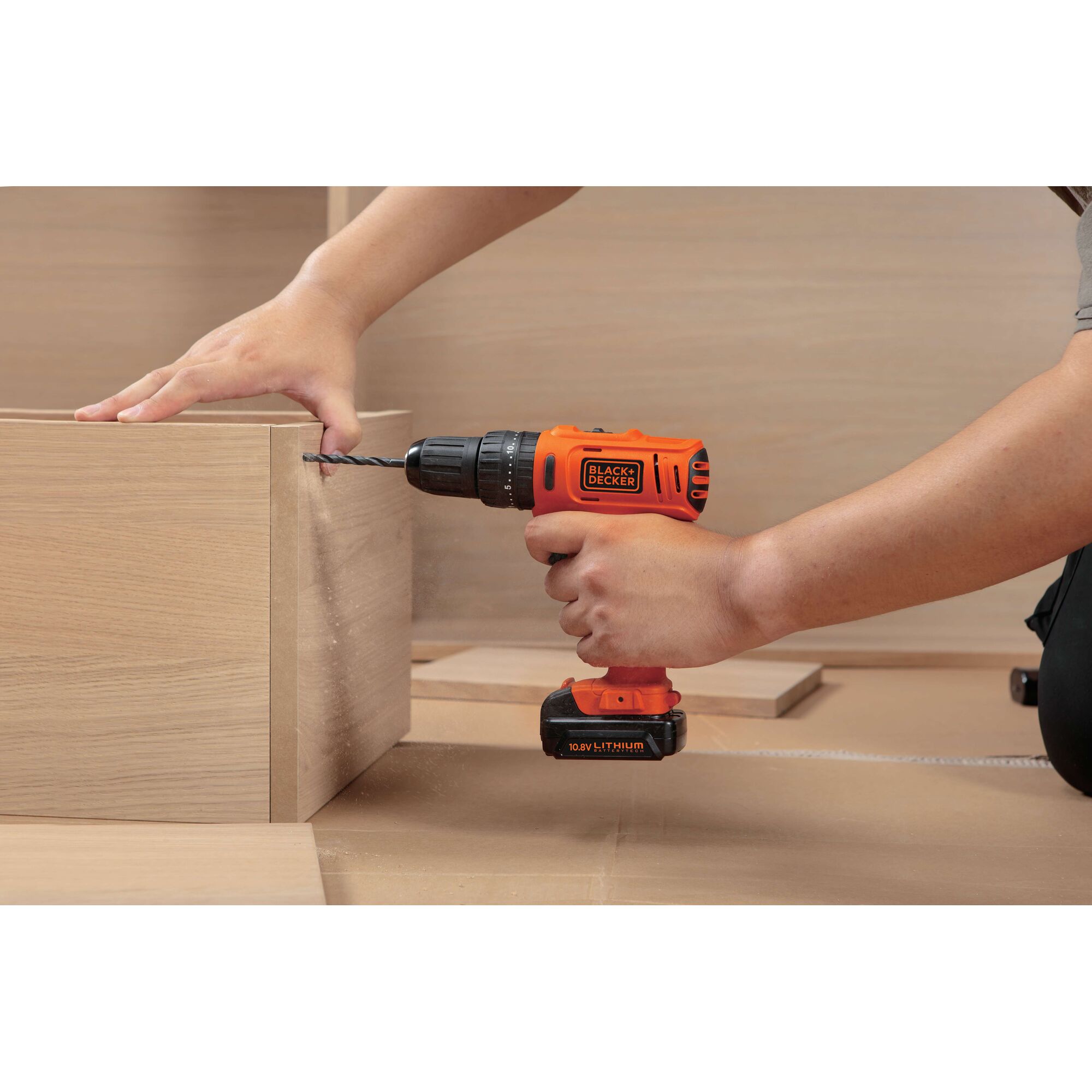 BLACKDECKER BDH12 cordless drill in use, orange color, drilling into light wood, side angle.