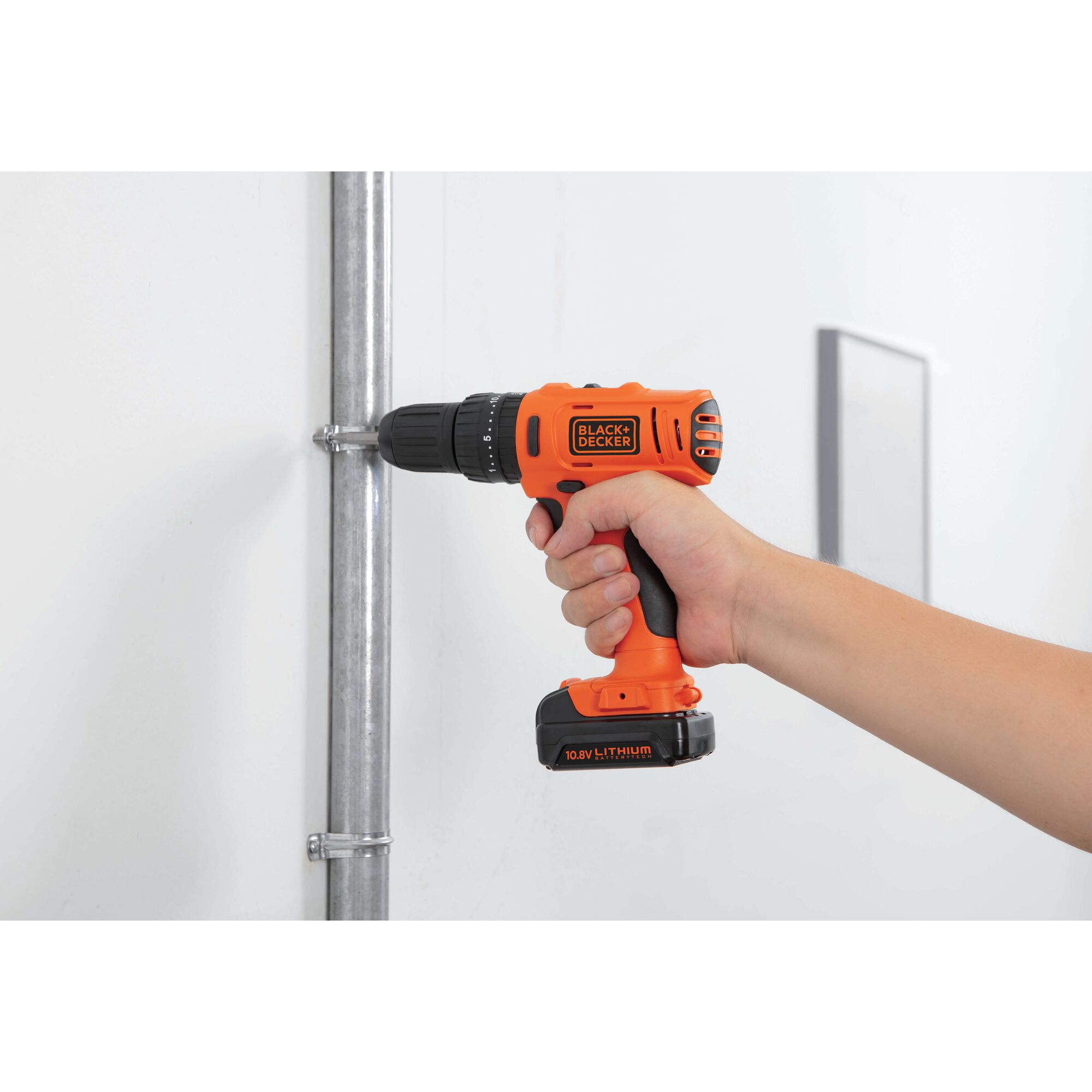 Photo of BLACKDECKER BDH12 cordless drill in use, orange and black, drilling into metal pipe indoors.