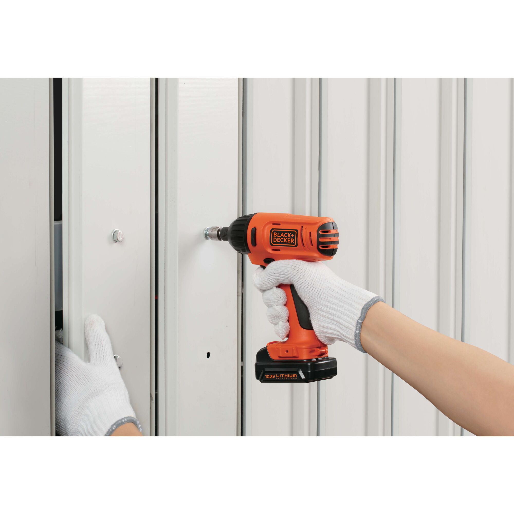 Photo of BLACKDECKER BDI12 cordless drill being used on a metal wall by gloved hands.