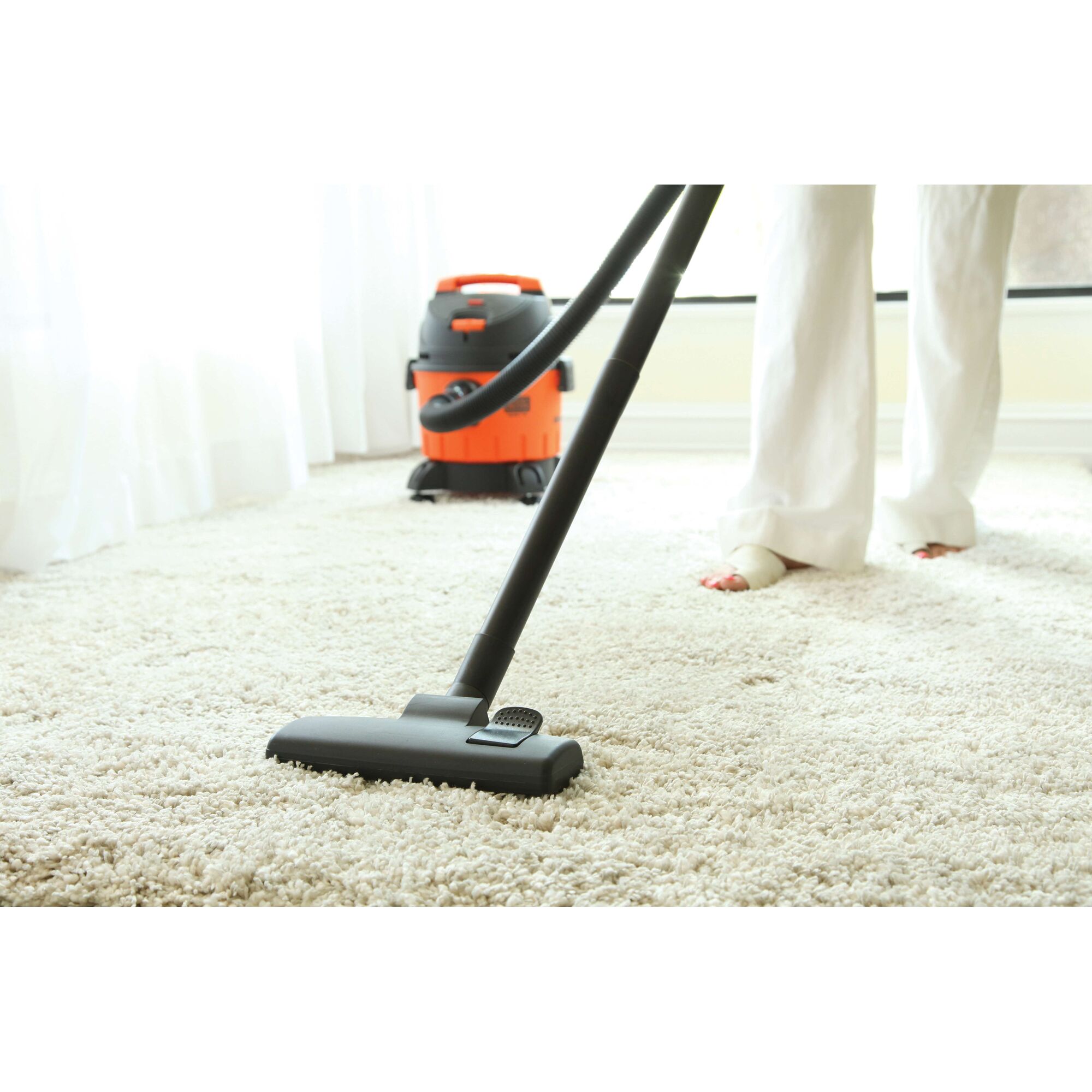 BLACKDECKER BDWD10 wet dry vacuum cleaning beige carpet, person in white pants visible.