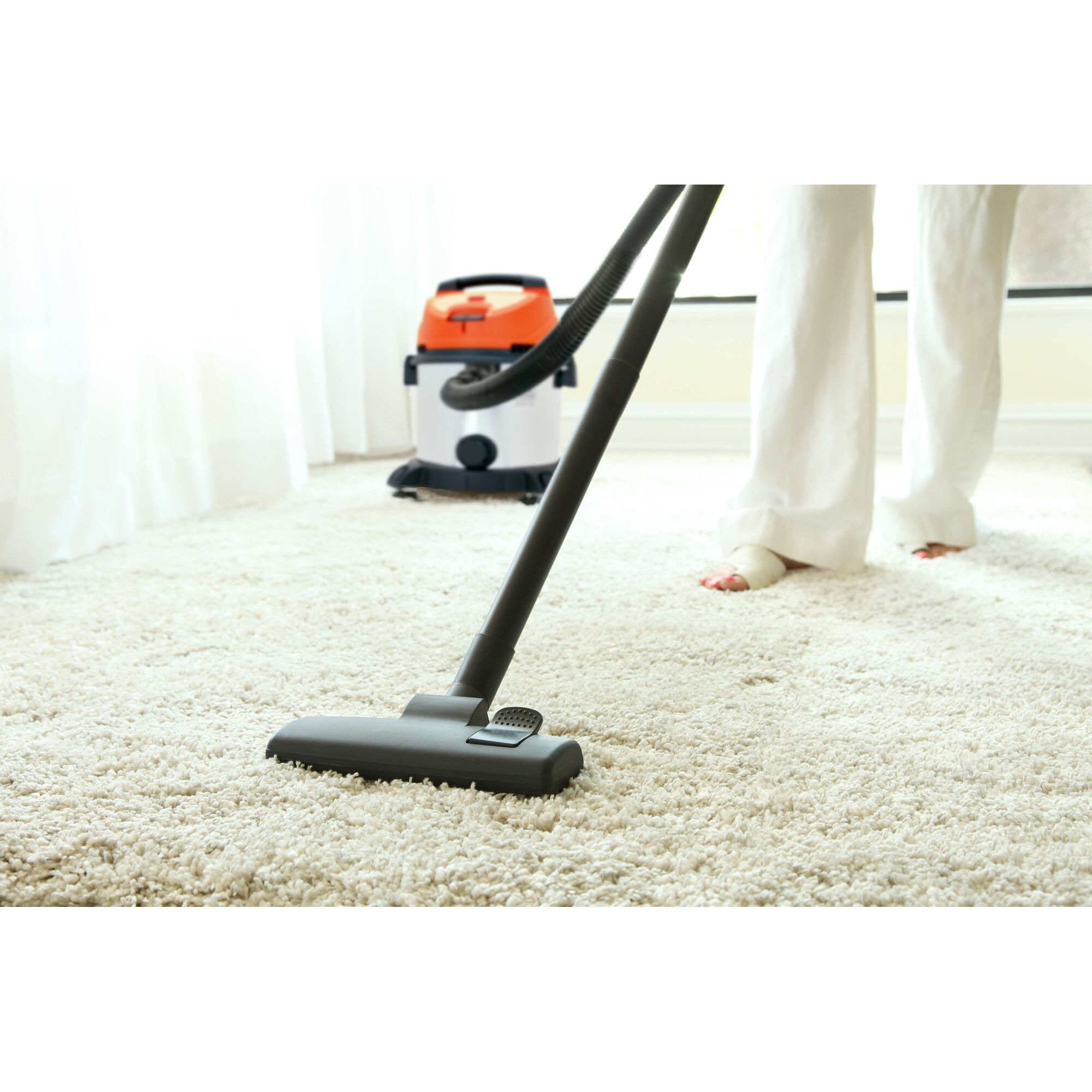Photo of BLACKDECKER BDWDS20 vacuum in use on a light carpet, orange and black canister in background.
