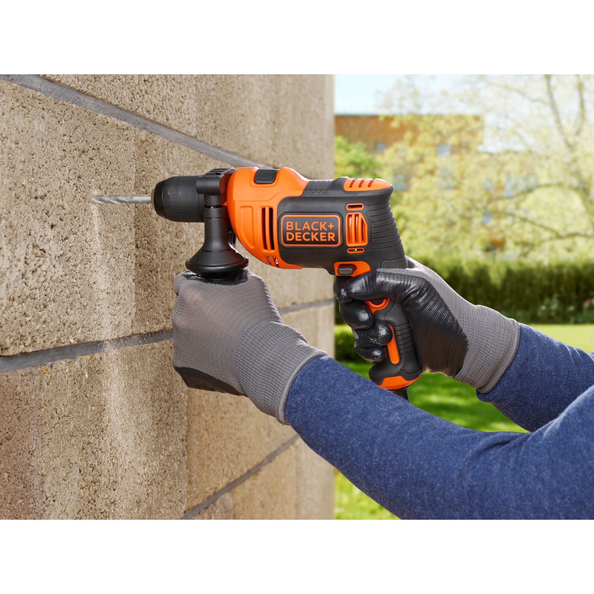 BLACK+DECKER BEH550 corded drill in use drilling into a concrete wall outdoors.