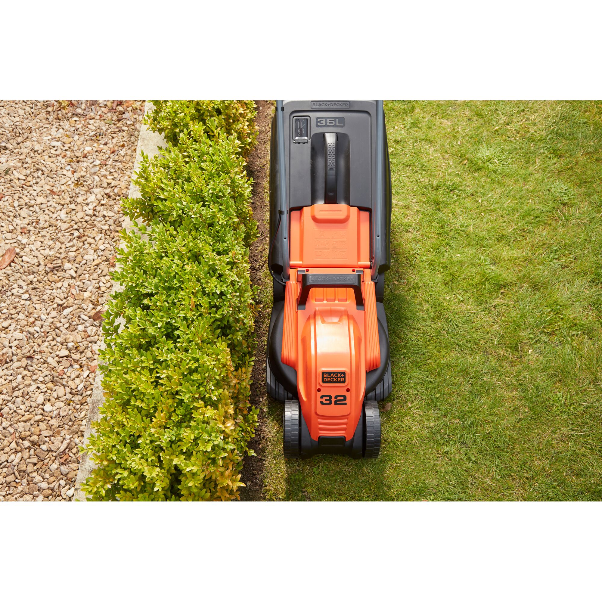 BLACK+DECKER BEMW451BH orange lawn mower top-view trimming grass along hedge.