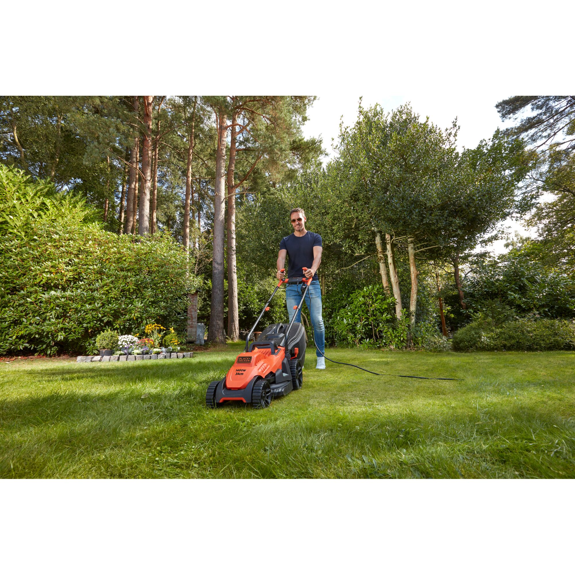 BLACKDECKER BEMW461BH lawn mower in use, orange body, user mowing grass in garden, outdoor scene.