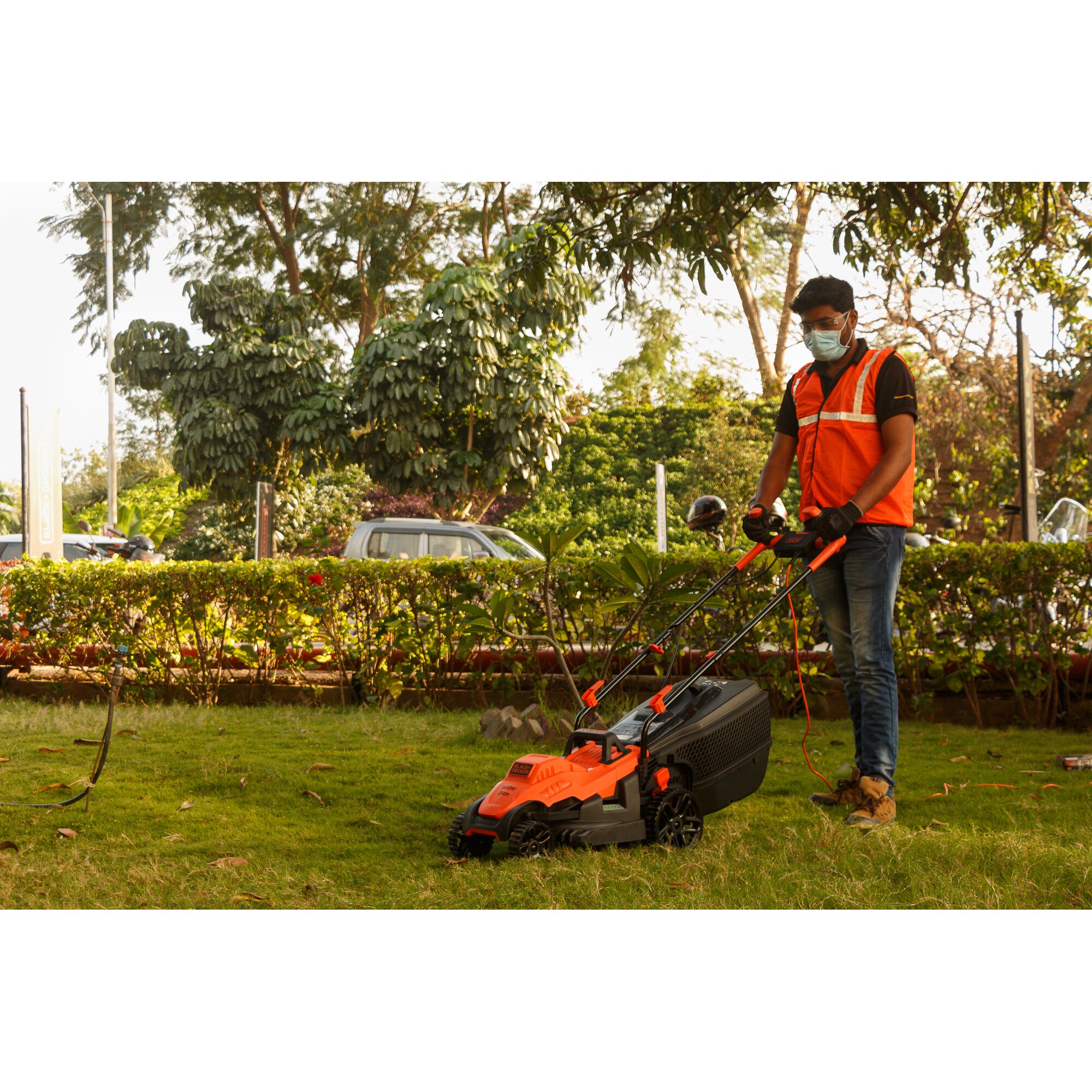 BLACKDECKER BEMW461BH lawn mower in use outdoors, orange and black color, grass cutting scene.