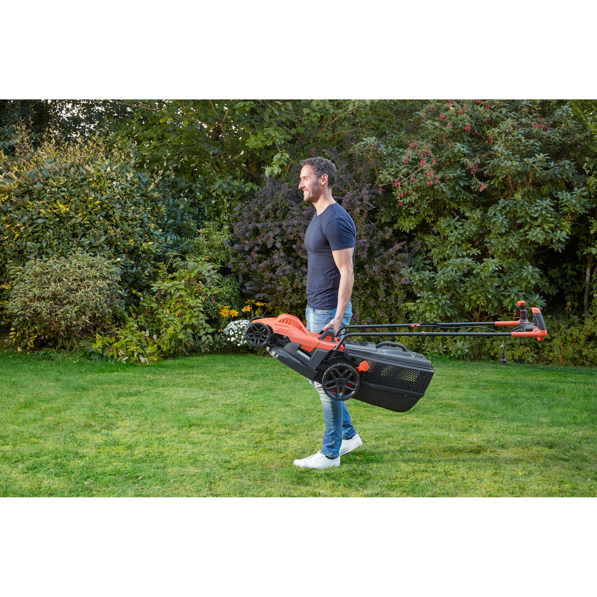 BLACKDECKER BEMW461BH lawn mower carried by person outdoors, orange and black design, garden setting.