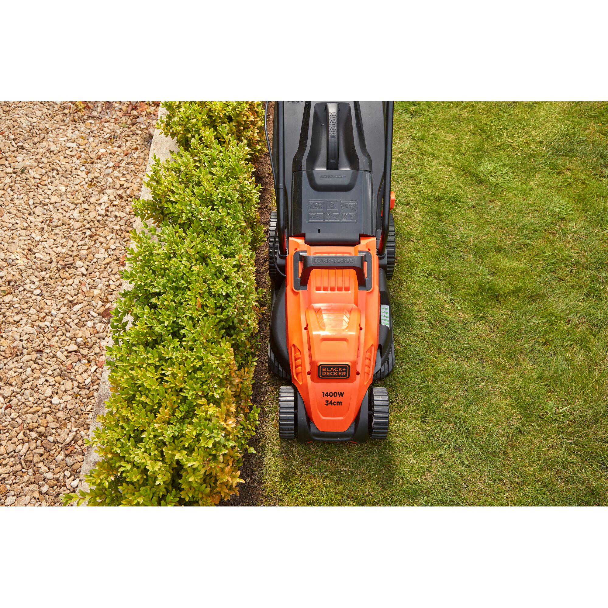 BLACK+DECKER BEMW461BH lawn mower top view cutting grass along hedge.