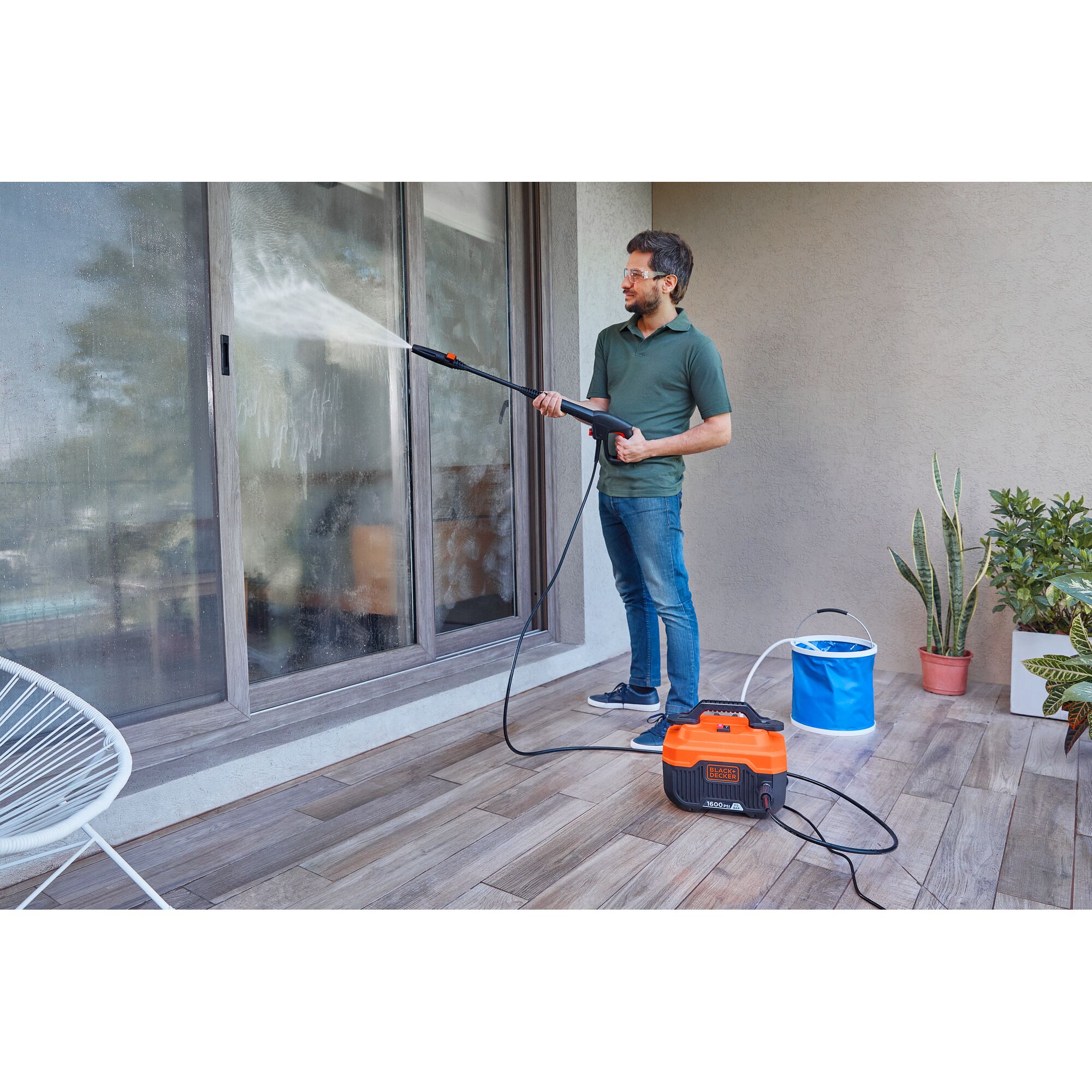 BLACKDECKER BEPW1600H pressure washer used outdoors to clean glass sliding doors, with plants nearby.