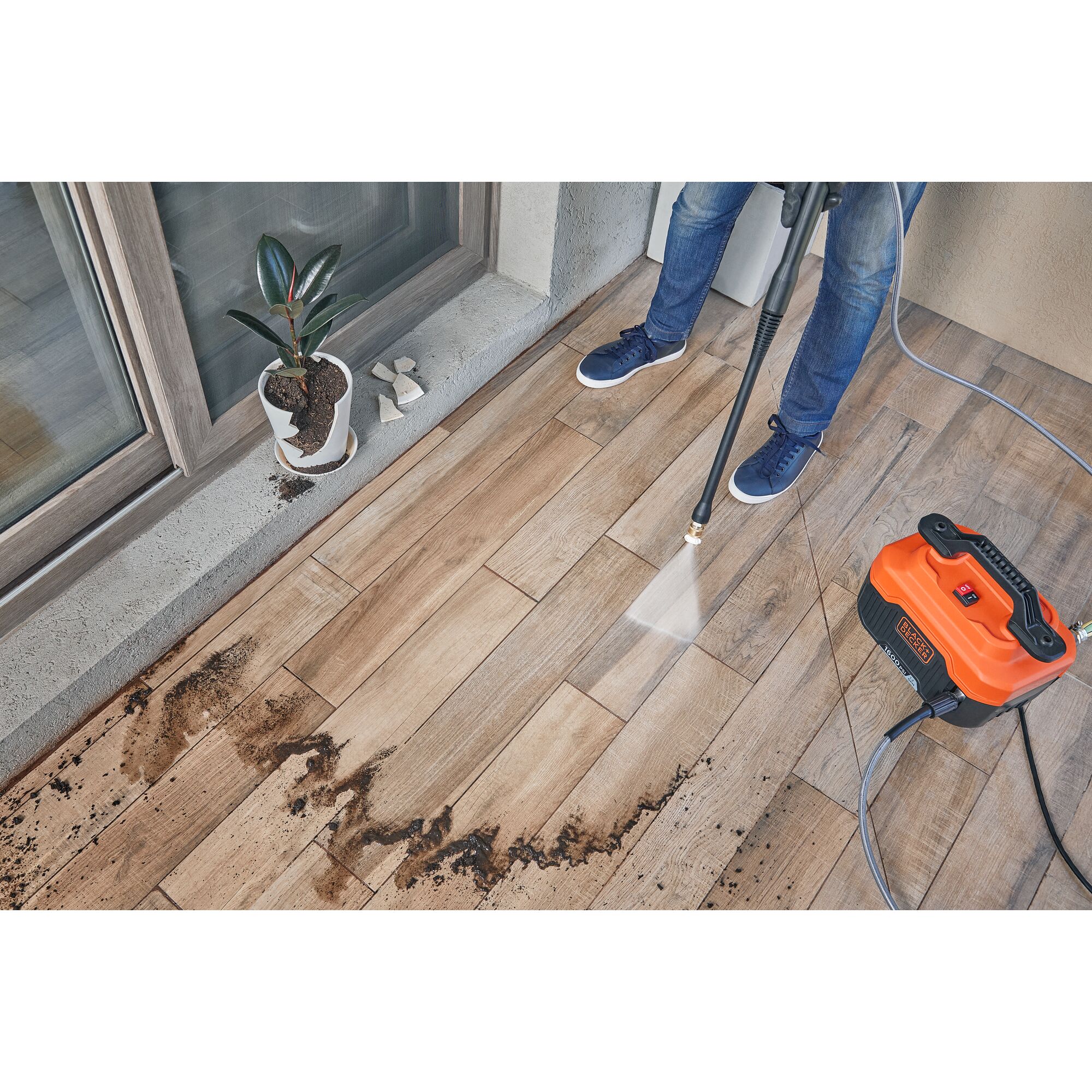 BLACKDECKER BEPW1600 pressure washer cleaning dirt from patio tiles, orange unit and water spray visible, top view.