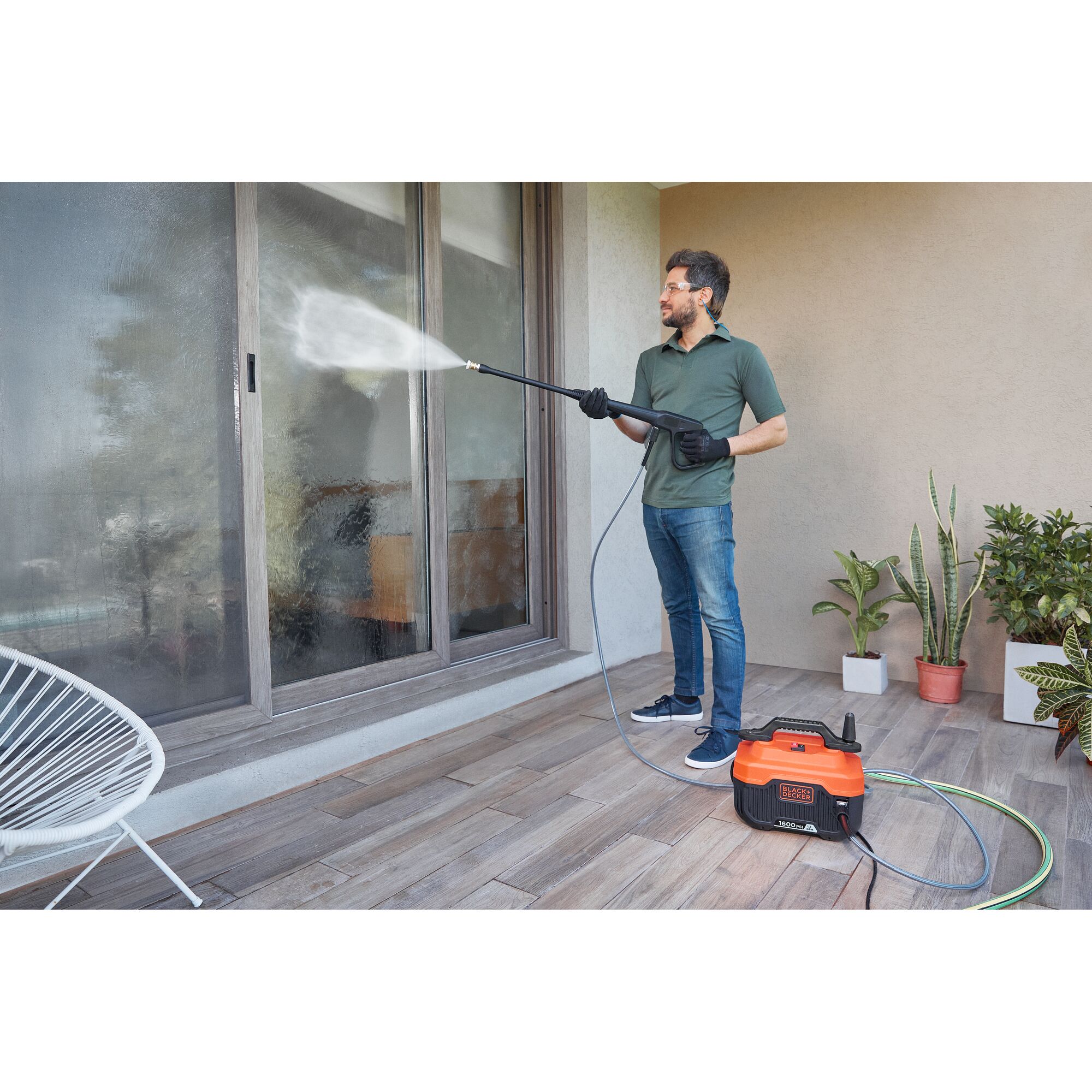 BLACKDECKER BEPW1600 pressure washer cleaning glass door on patio, person holding spray wand, plants in background.
