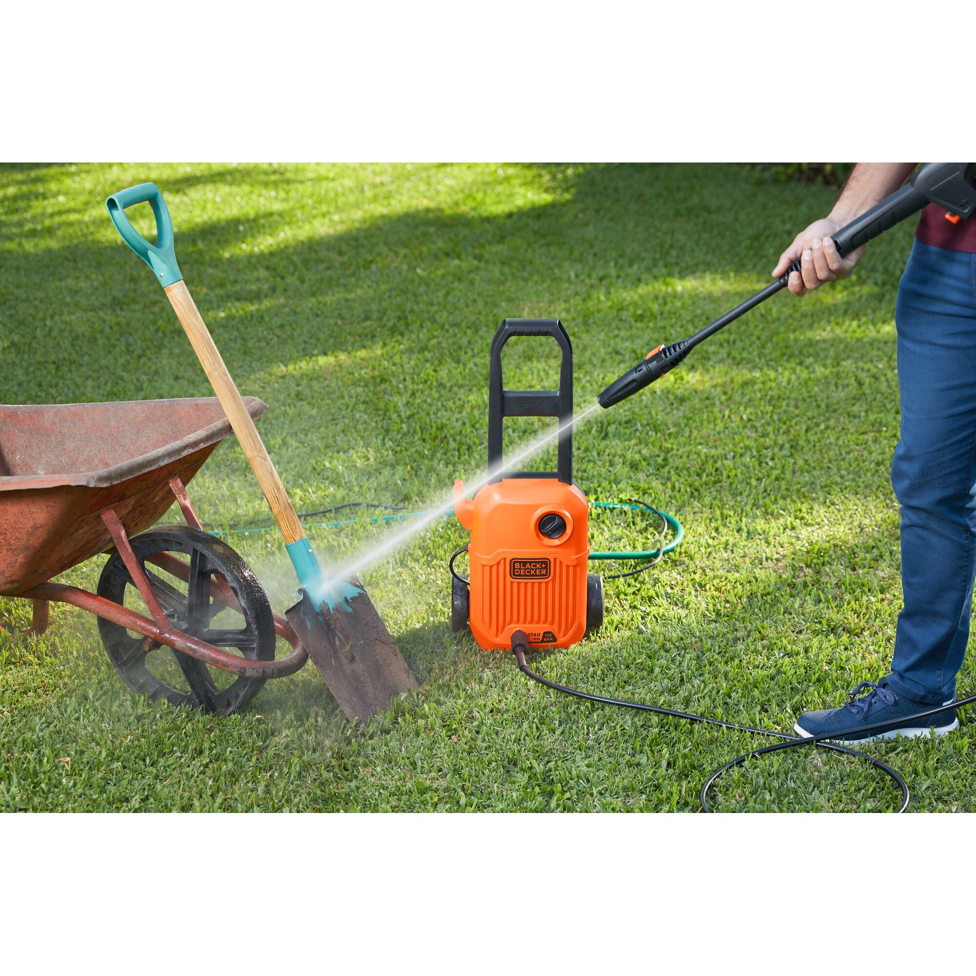 BLACKDECKER BEPW1750 pressure washer cleaning a garden shovel outdoors, with wheelbarrow visible.