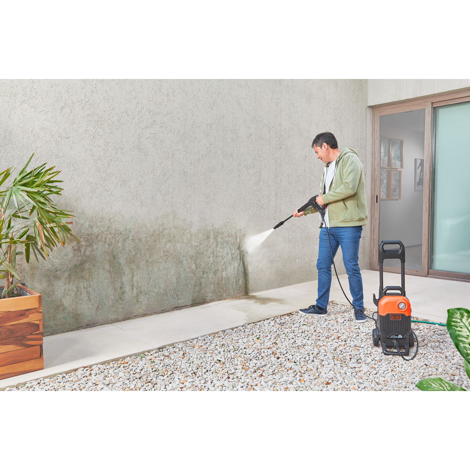 BLACKDECKER BEPW2200 pressure washer cleaning outdoor wall, person using sprayer in garden setting.
