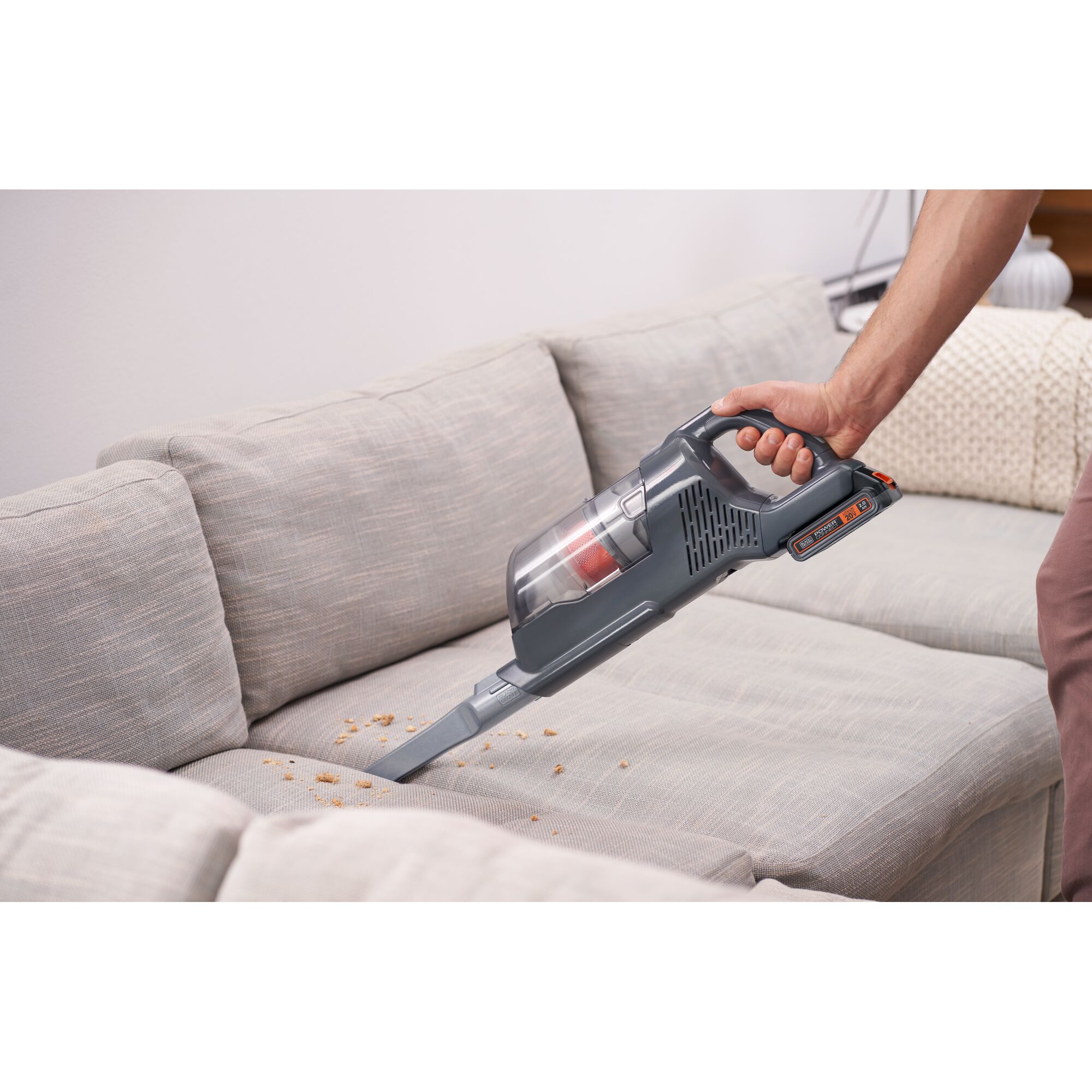 BLACKDECKER BHFEA18D1 handheld vacuum cleaner cleaning crumbs on light gray sofa upholstery.