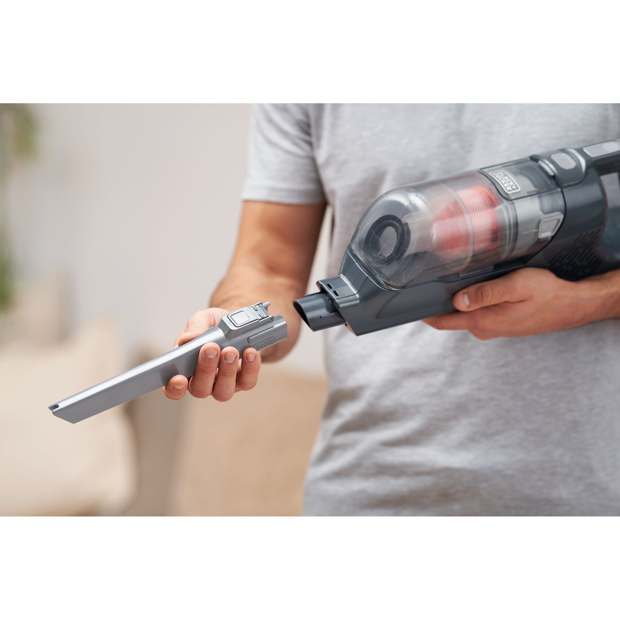 A person is attaching a nozzle accessory to a BLACK+DECKER handheld vacuum cleaner.