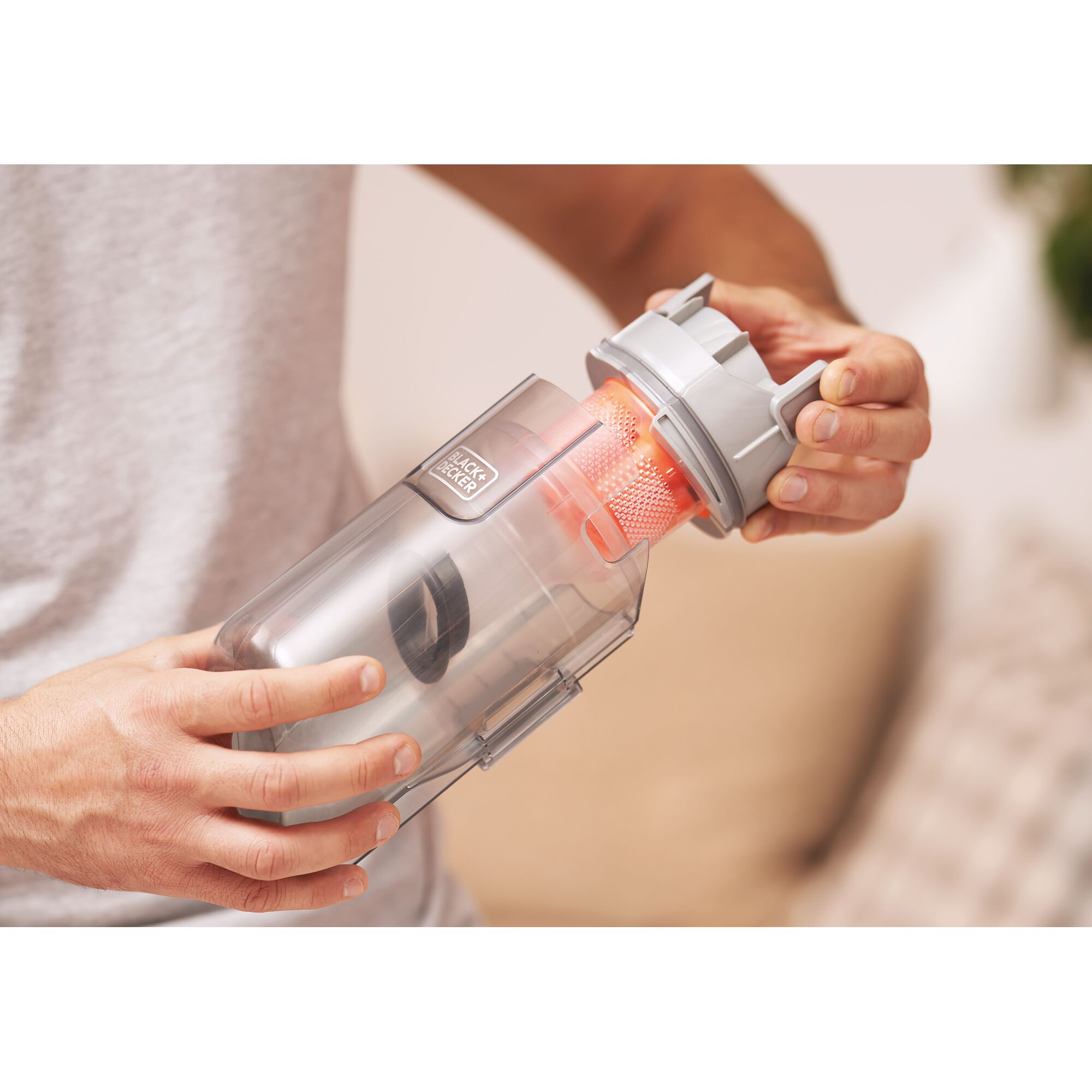 Close-up of a person holding and removing the filter from a transparent dust container of a BLACK+DECKER cordless vacuum cleaner.