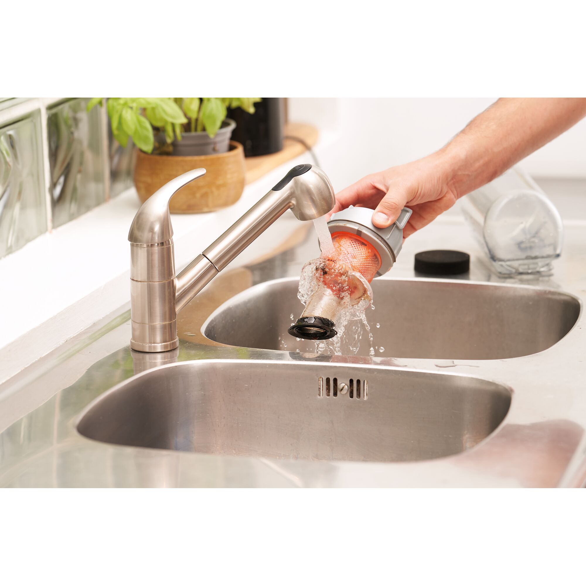 A person rinses the filter and dust container from a BLACK+DECKER vacuum cleaner under a kitchen sink faucet.