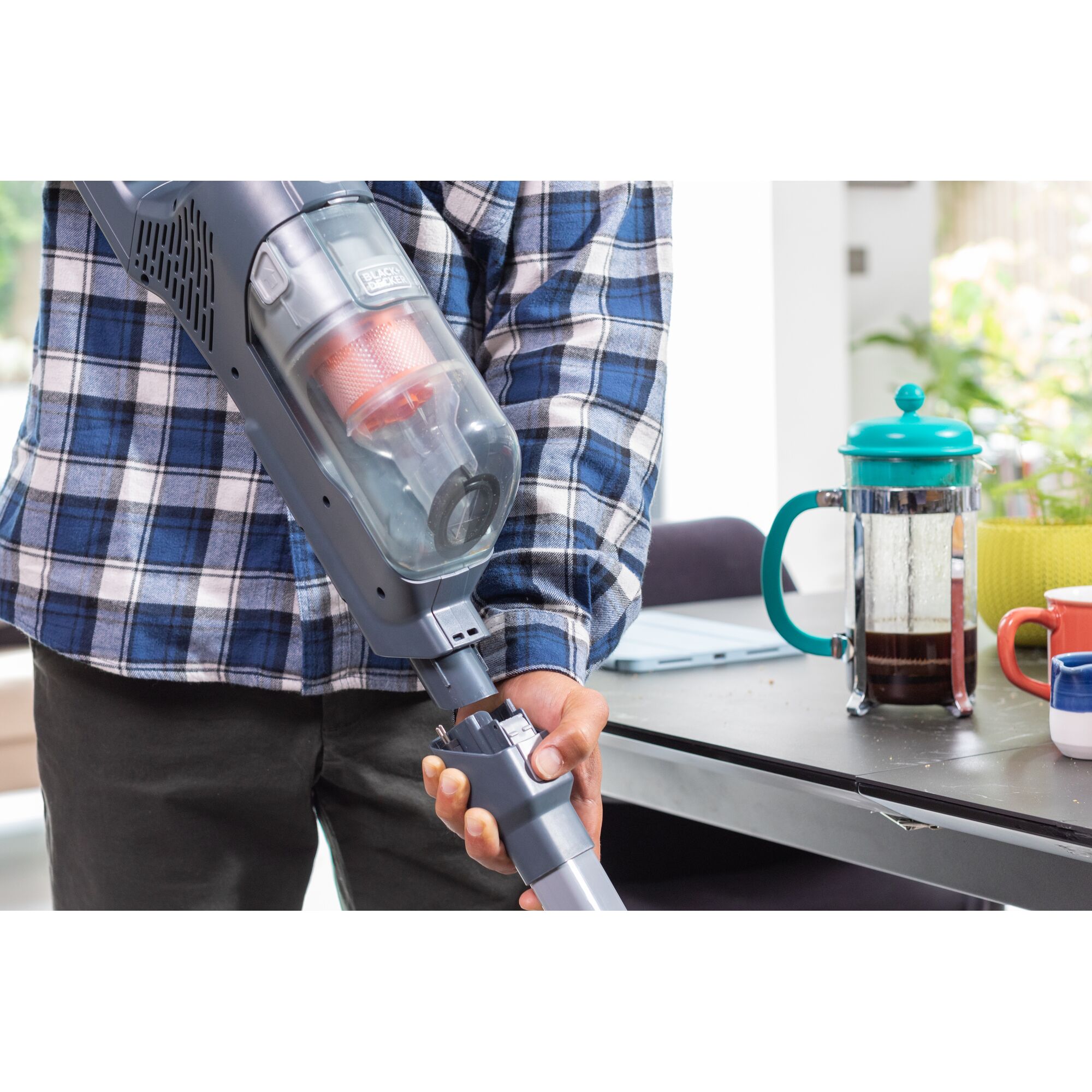 BLACKDECKER BHFEA520J cordless vacuum cleaner held near coffee table with French press and mugs.