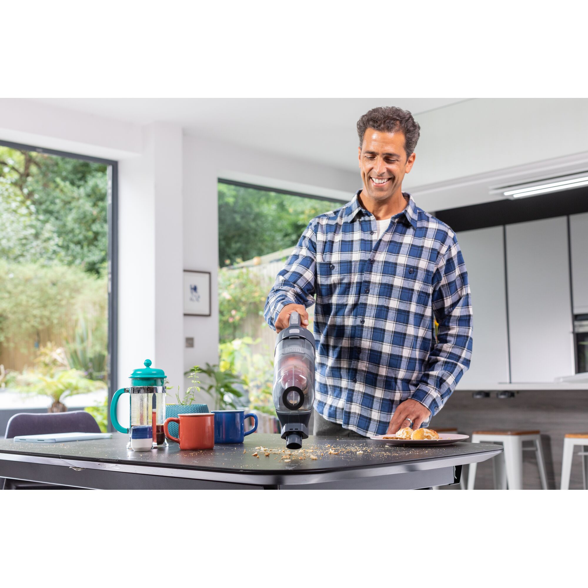 BLACKDECKER BHFEA520J cordless vacuum cleaning crumbs on a kitchen table near mugs and a French press.