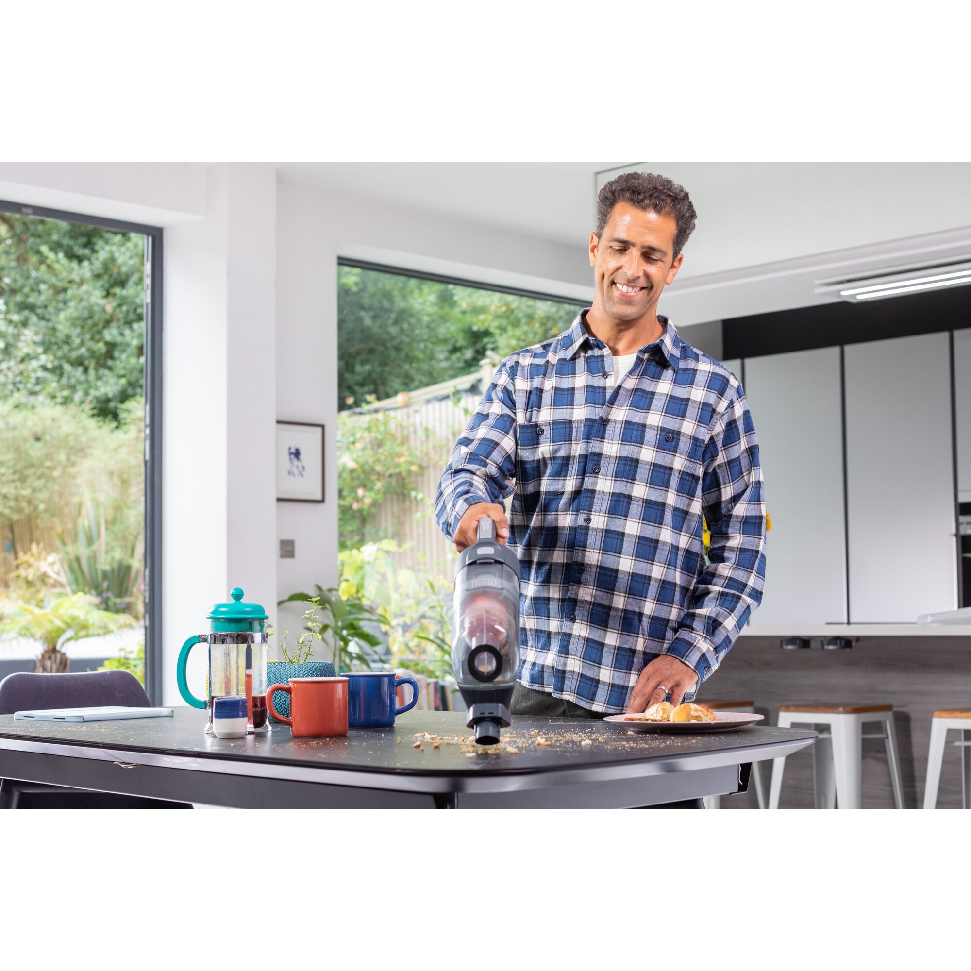 BLACKDECKER BHFEA520J handheld vacuum in use cleaning crumbs on kitchen table near cups and coffee press.