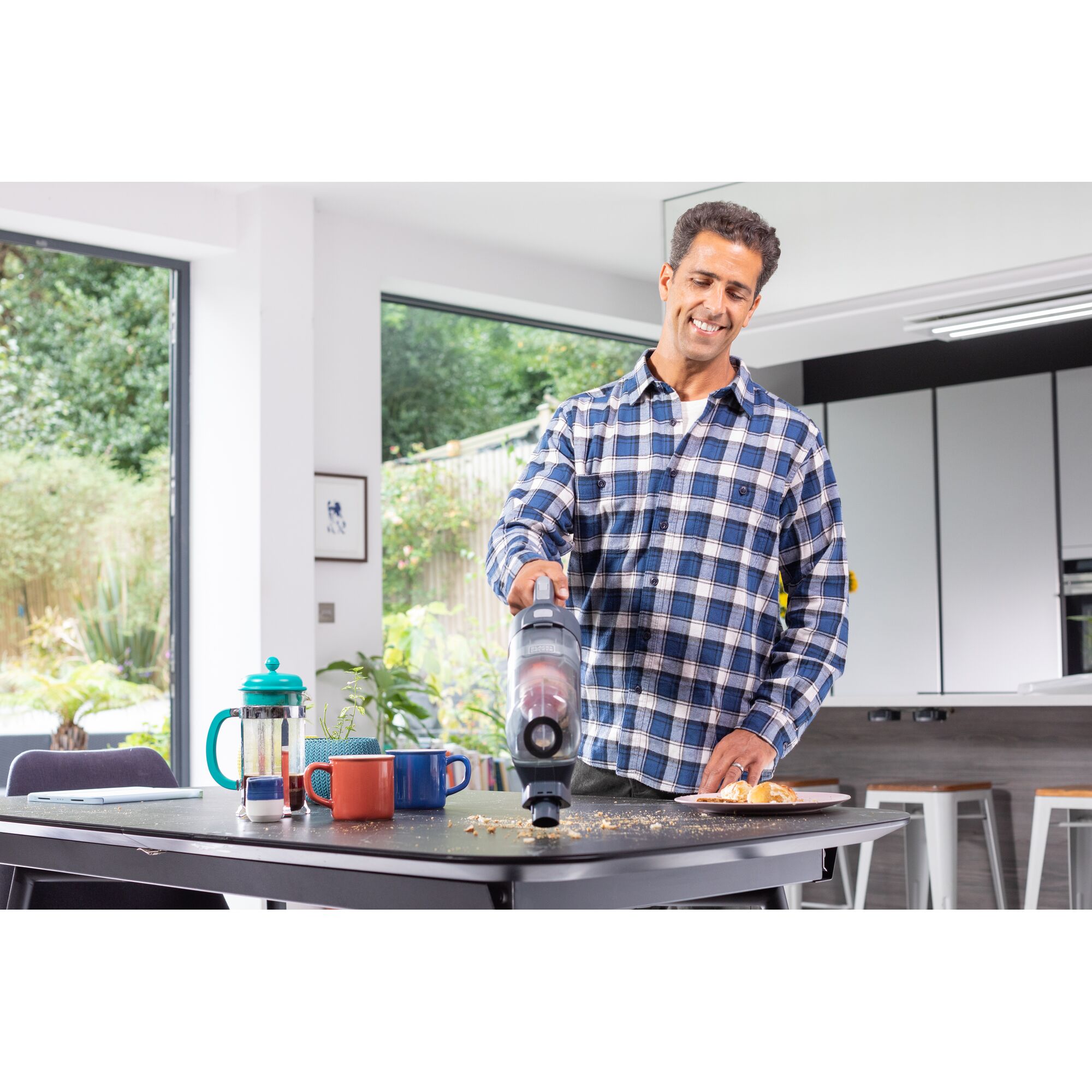 BLACKDECKER BHFEA520J cordless handheld vacuum cleaning crumbs from kitchen table next to mugs and French press.