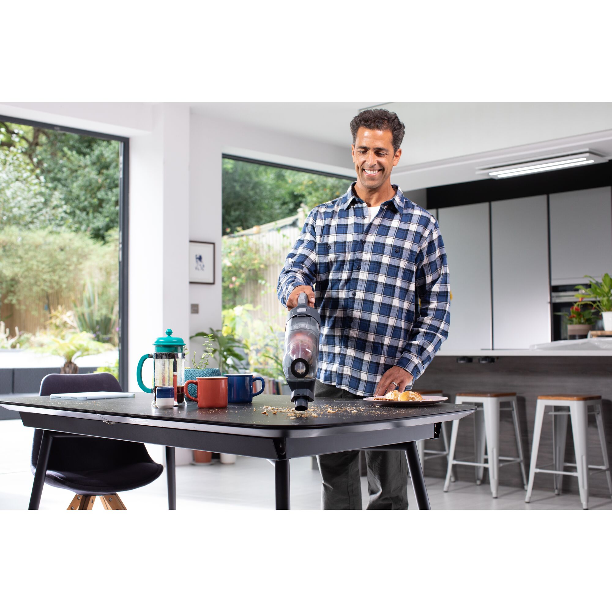 BLACKDECKER BHFEA520J handheld vacuum cleaning crumbs from kitchen table with mugs and French press.