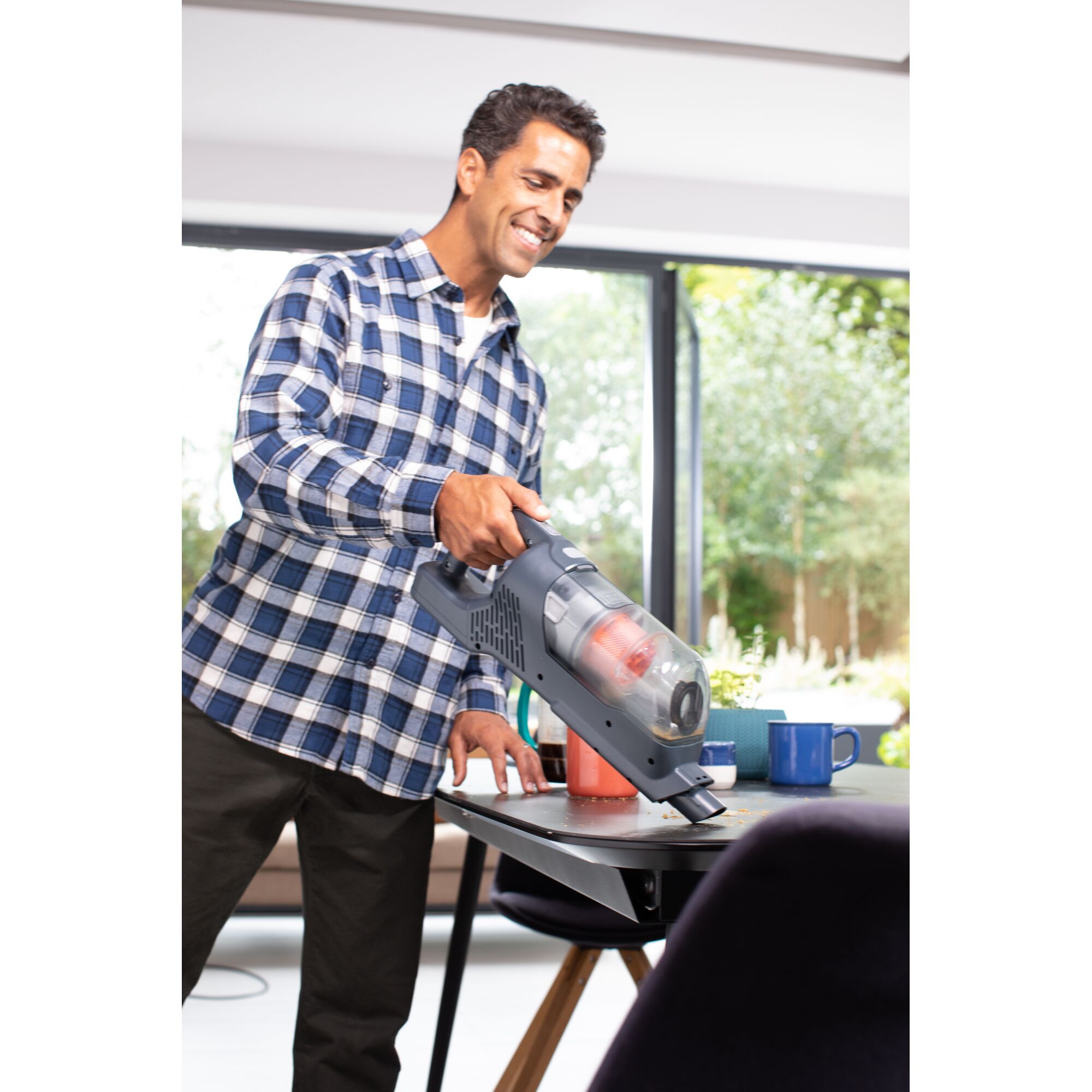 Photo of person using BLACKDECKER BHFEA520J handheld vacuum to clean tabletop near colored mugs indoors.