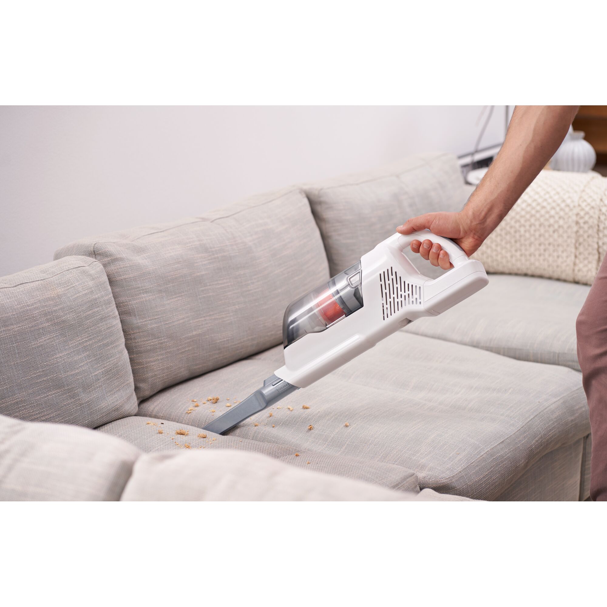 BLACKDECKER BHFEA520J handheld vacuum cleaning crumbs from light gray sofa upholstery.